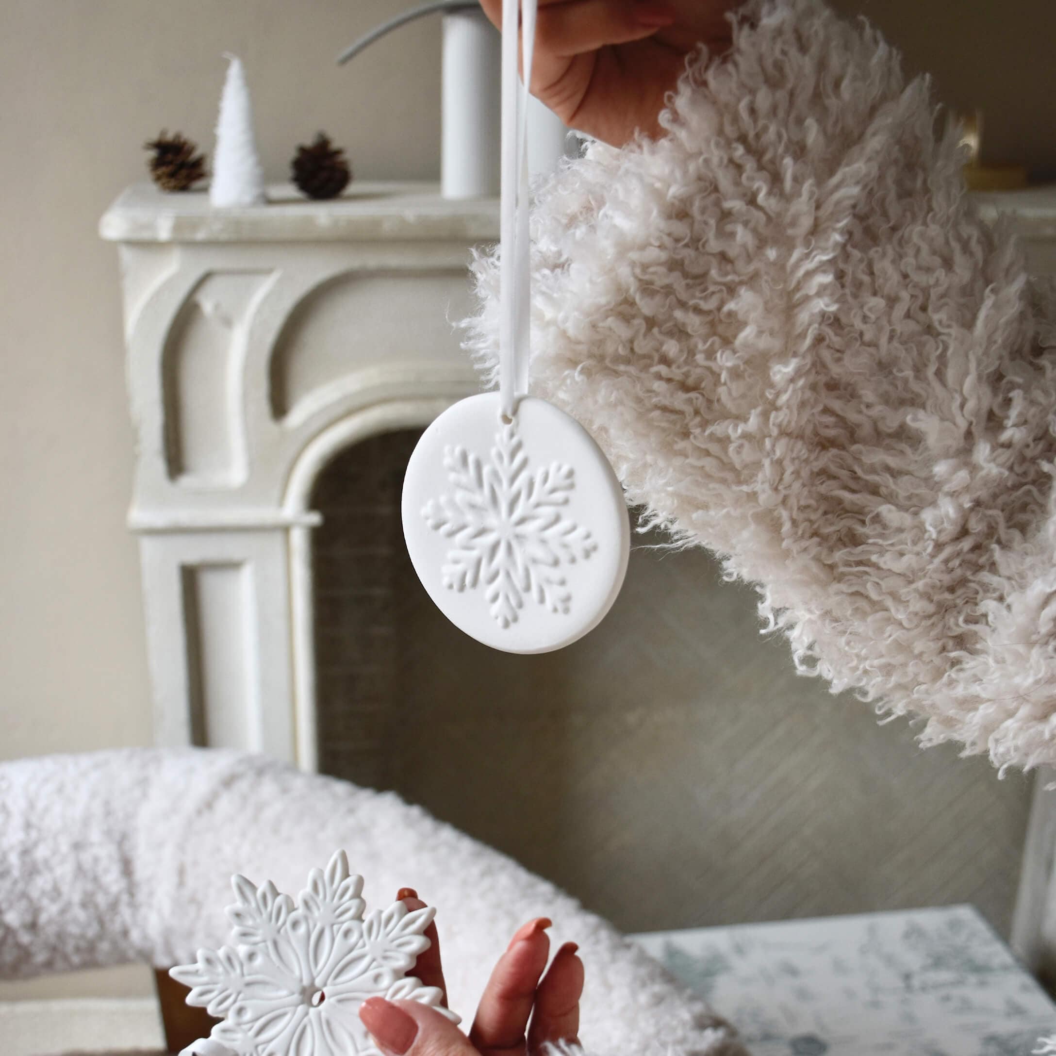 Décorations de Noël en céramique blanche avec motif flocon de neige, tenue devant une cheminée et un pull doux