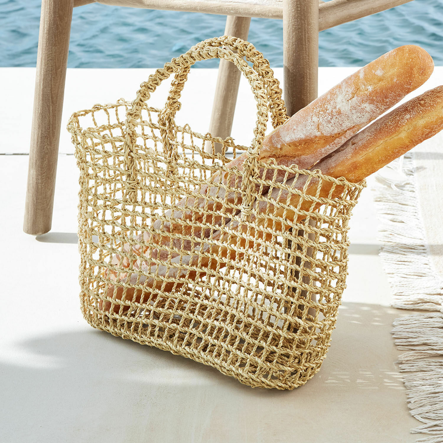 Panier Xaintieux Sac filet naturel en matériau tressé avec deux baguettes posé près d'un tabouret en bois