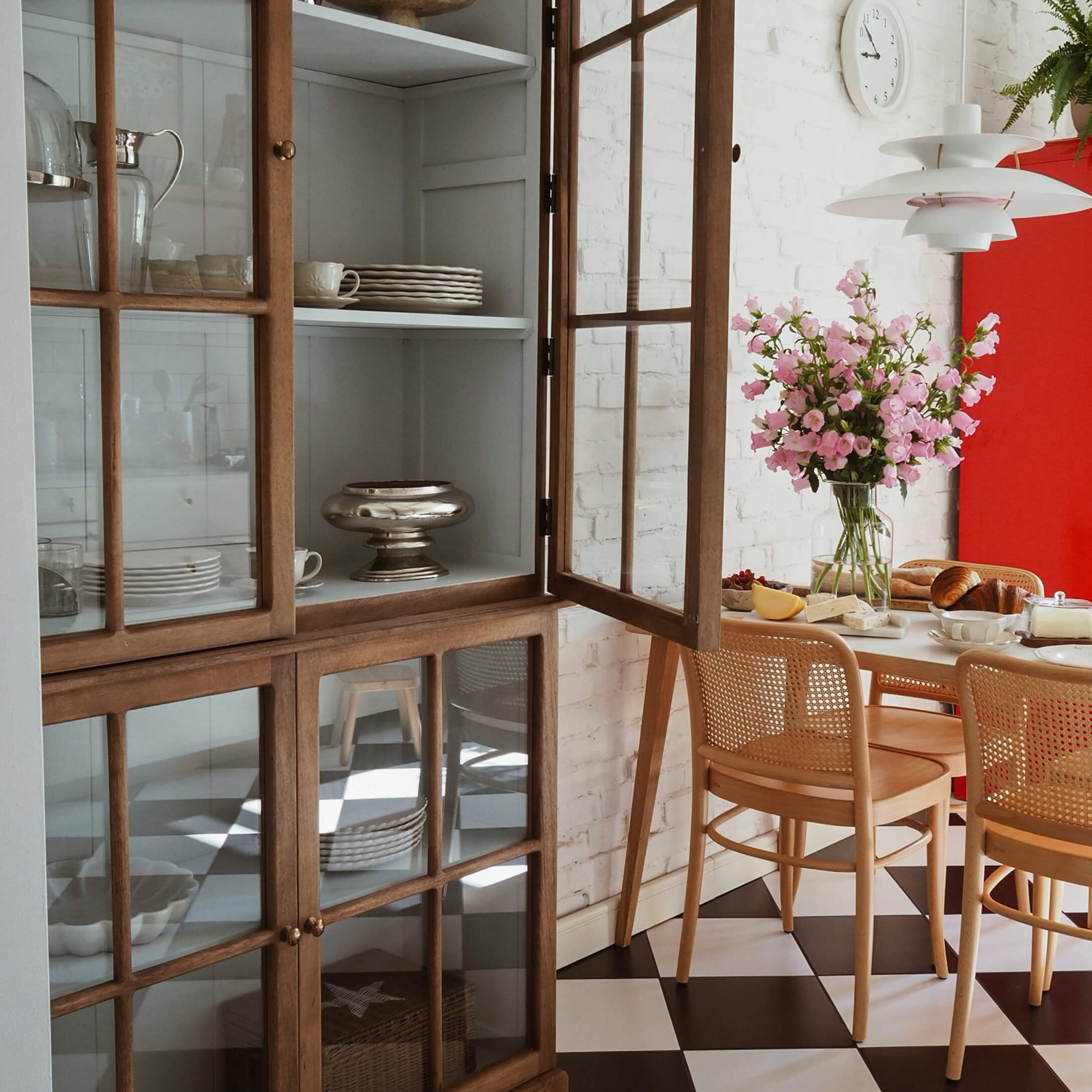 Salle à manger lumineuse avec vitrine en bois, fleurs roses et sol à carreaux noir et blanc