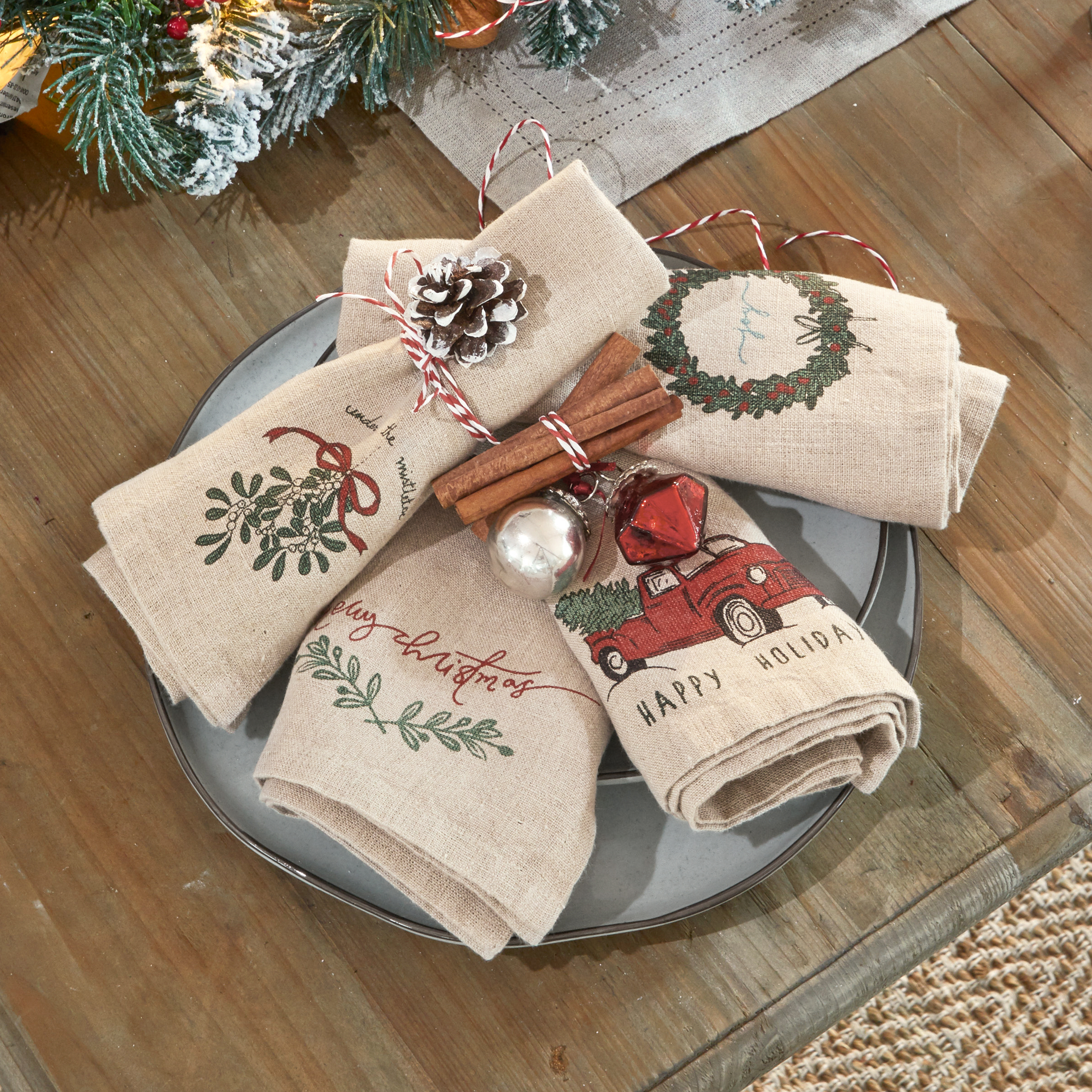 Serviettes en lin beige avec motifs de Noël, décorées de bâtons de cannelle et pomme de pin sur assiette grise
