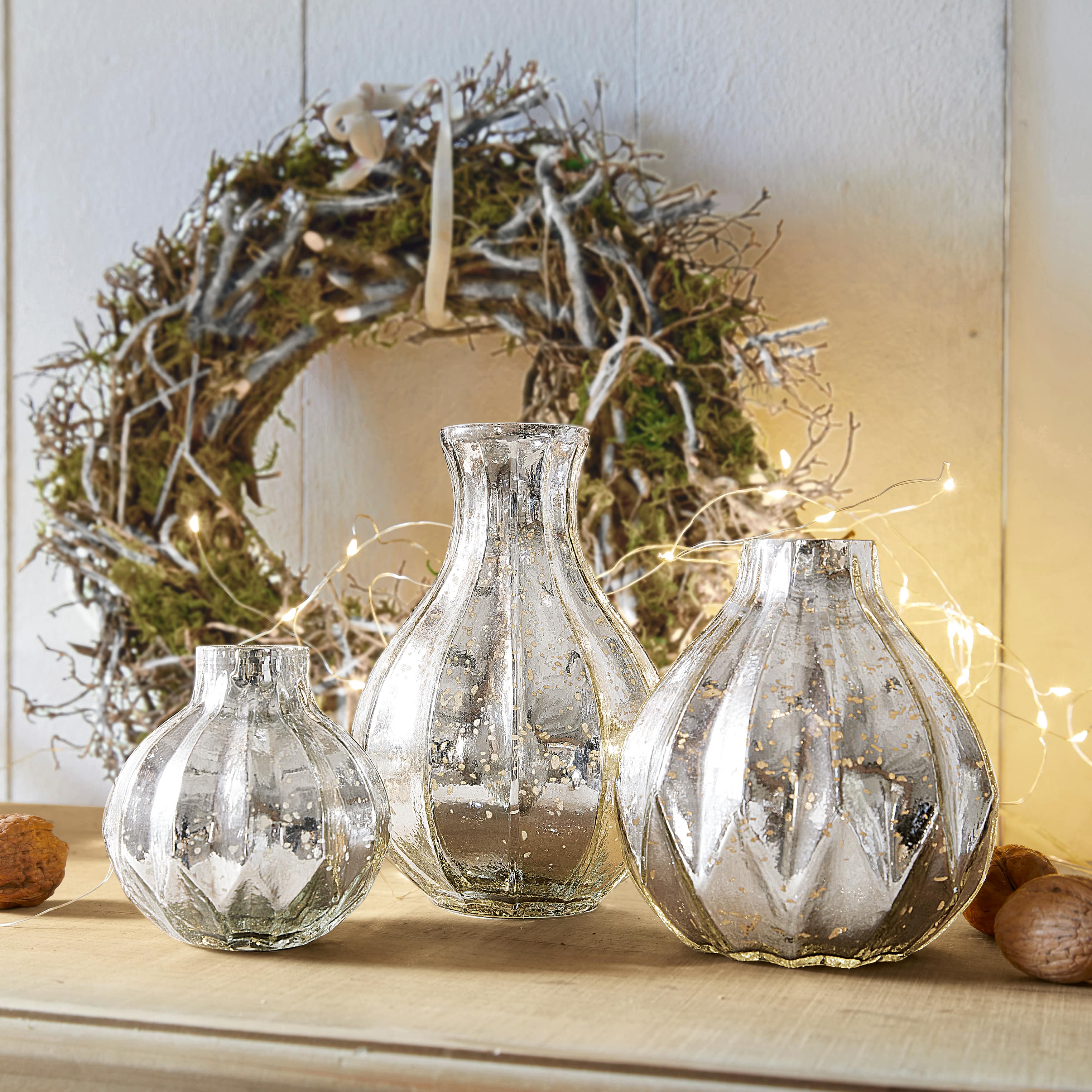 Ensemble de trois vases décoratifs en verre argenté avec effet vieilli posés sur une table en bois