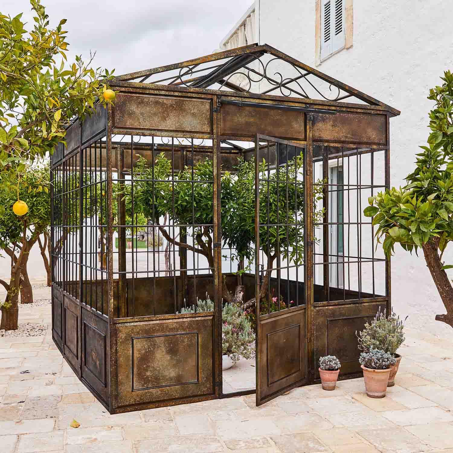 Kiosque de jardin en métal vieilli avec plantes et citronniers sur une terrasse en pierre