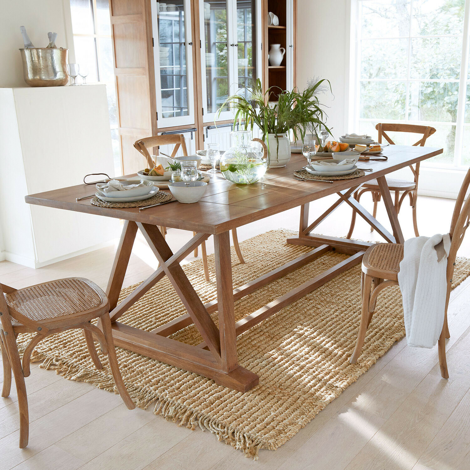 Table à manger en bois avec chaises et tapis naturel dans une pièce lumineuse décorée pour repas
