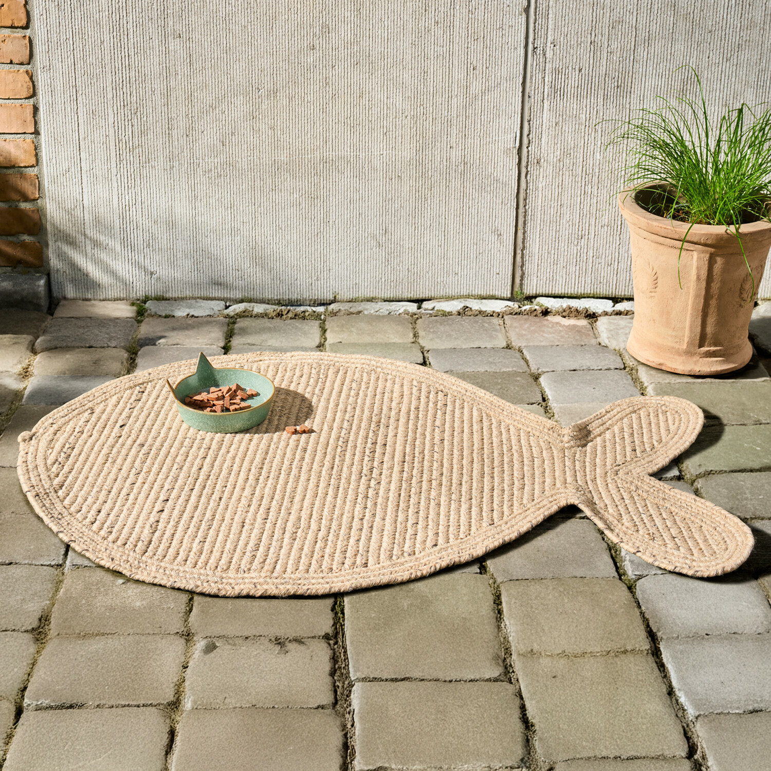 Tapis en forme de poisson en corde naturelle beige posé sur un sol en pavés gris
