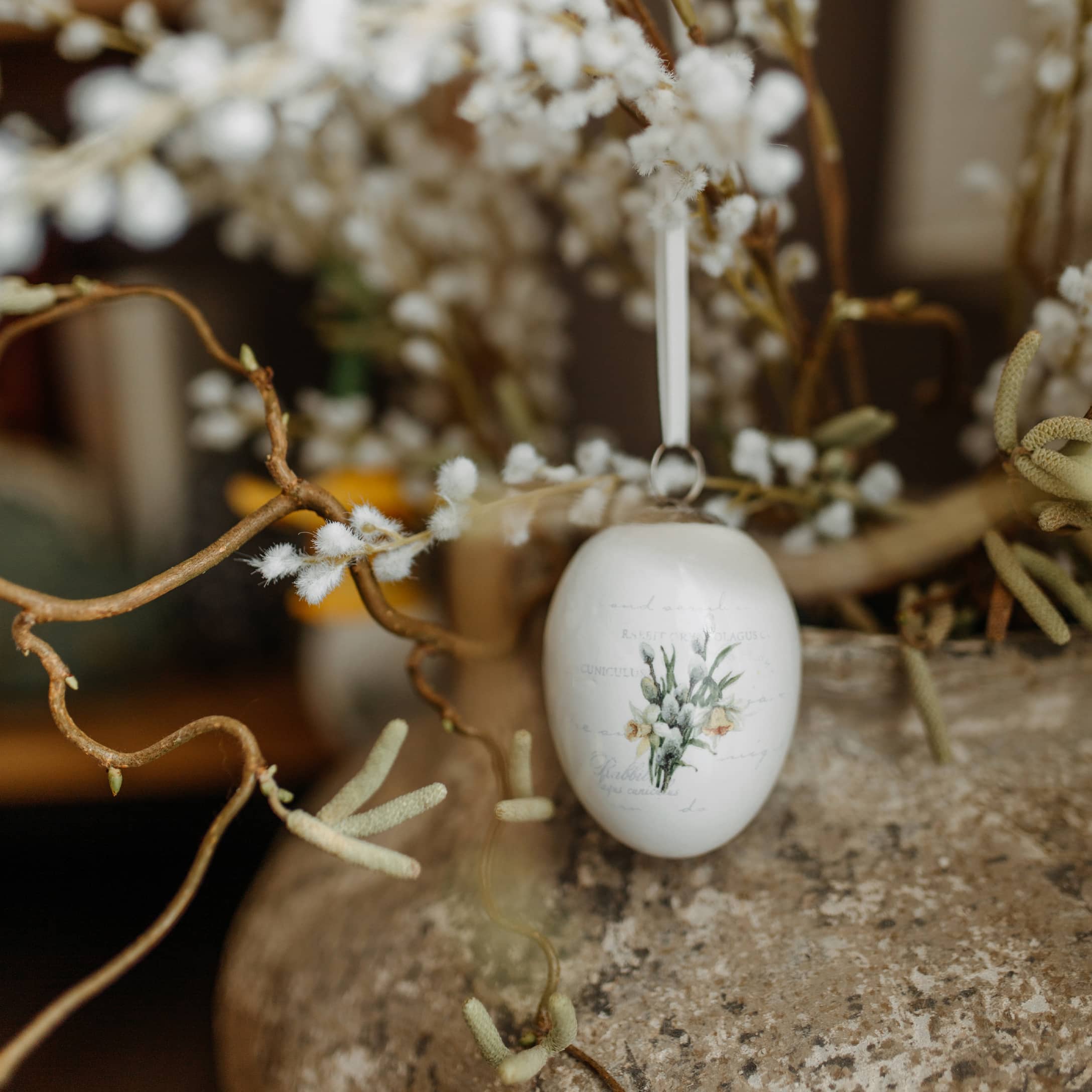 Décoration de Pâques en céramique blanche avec motif floral suspendue à une branche aux bourgeons duveteux