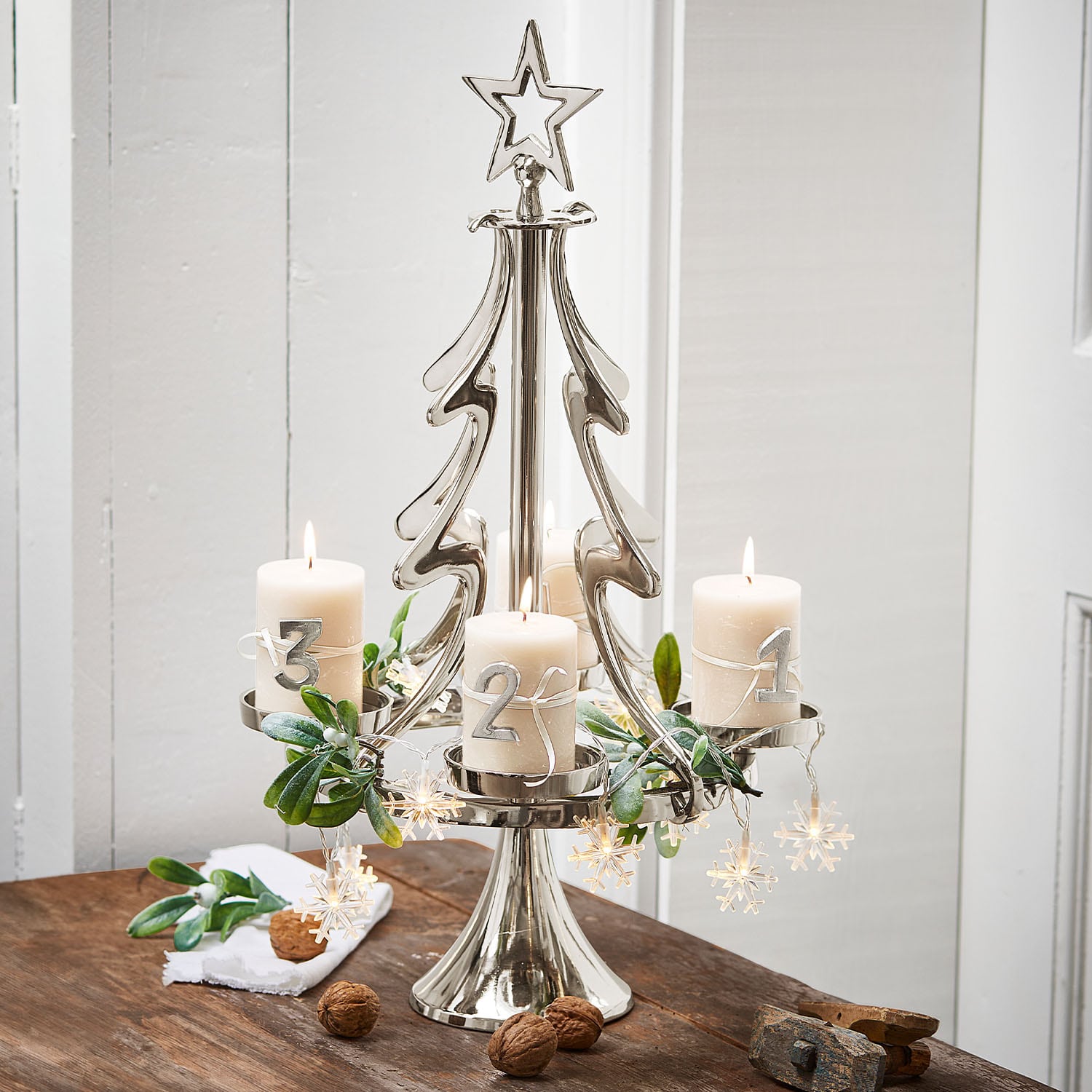 Bougeoir en métal en forme de sapin avec quatre bougies blanches et décoration de Noël sur une table en bois
