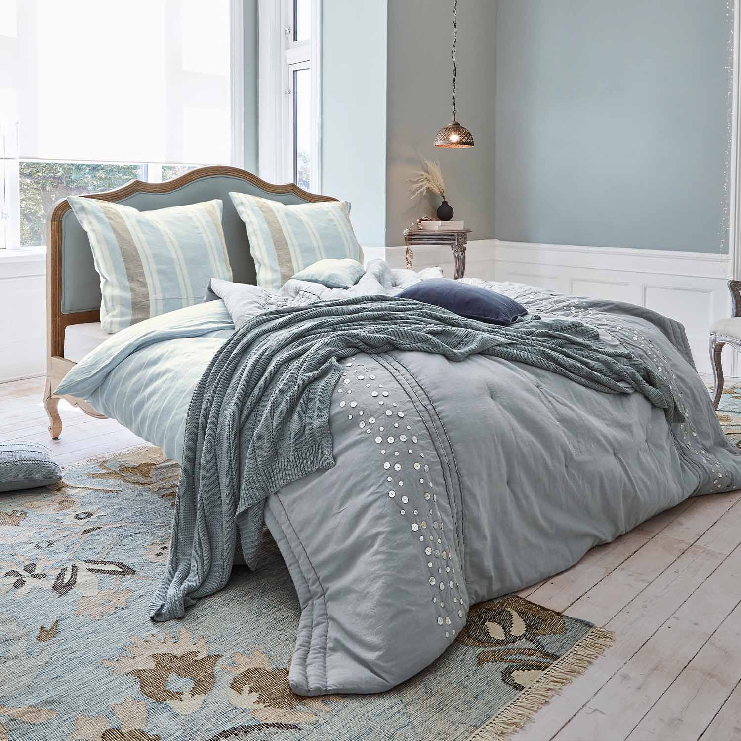 Lit en bois avec tête de lit rembourrée et linge de lit bleu clair avec couverture tricotée douce