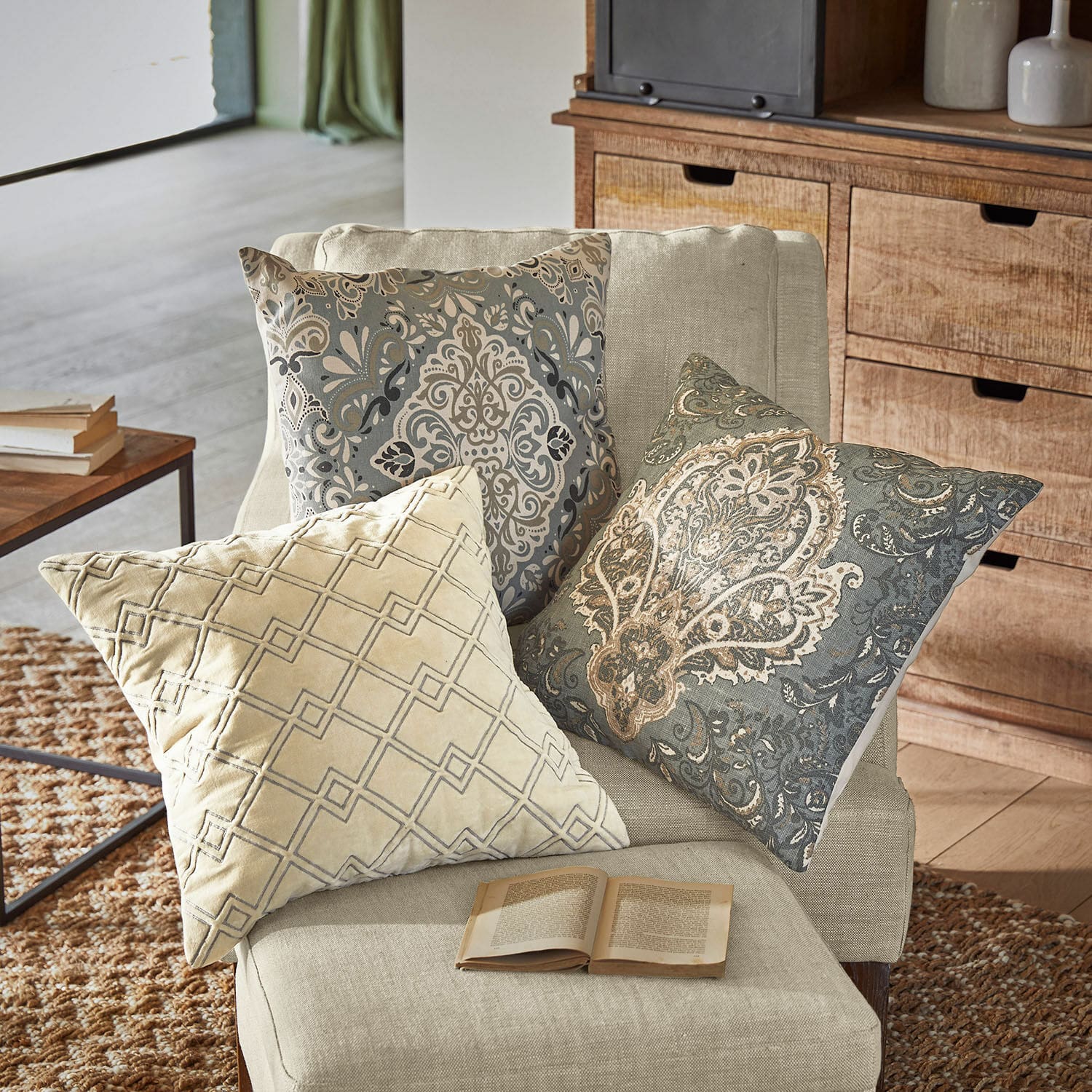 Lot de 3 housses de coussins Madalena Trois coussins décoratifs beige et gris avec motifs sur un fauteuil clair dans un salon cosy