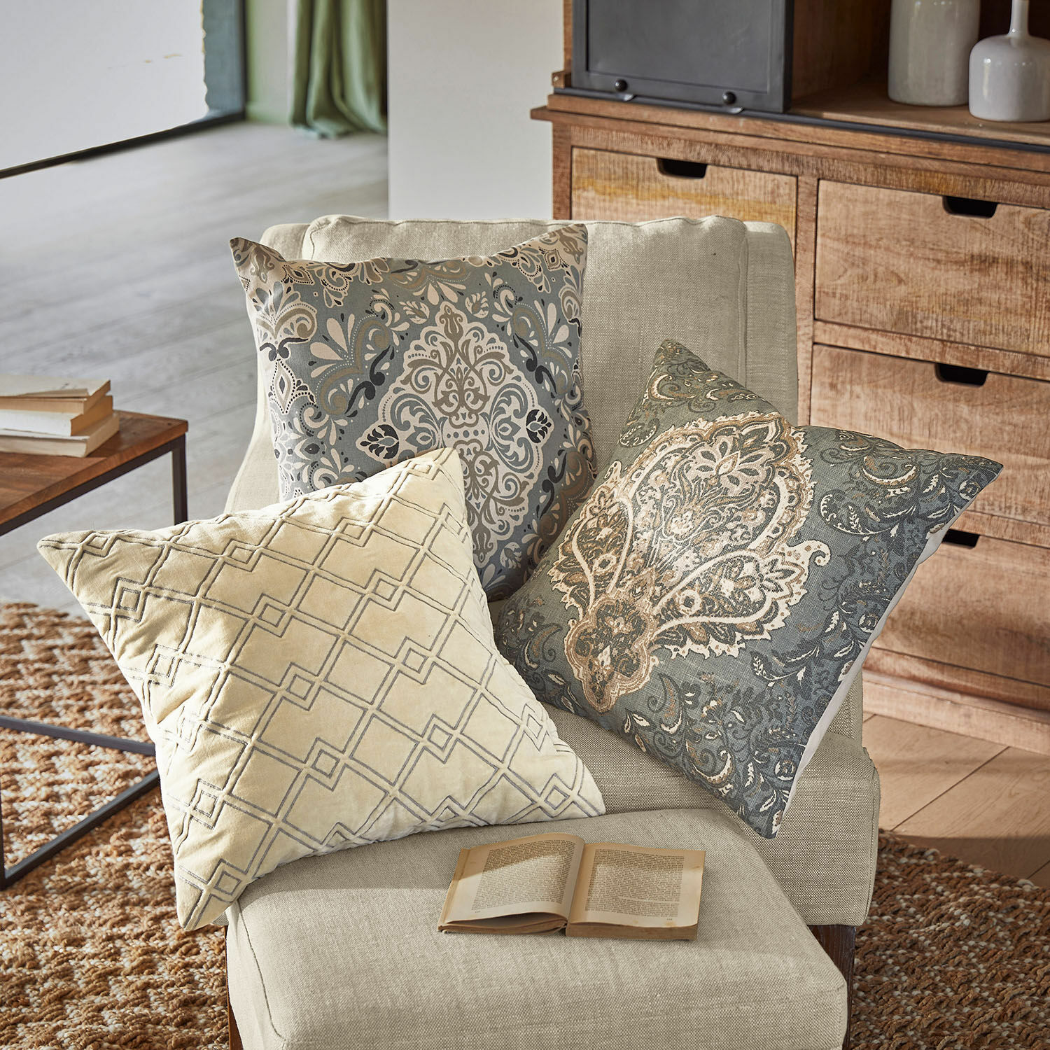 Lot de 3 housses de coussins Madalena Trois coussins décoratifs beige et gris avec motifs sur un fauteuil clair dans un salon cosy