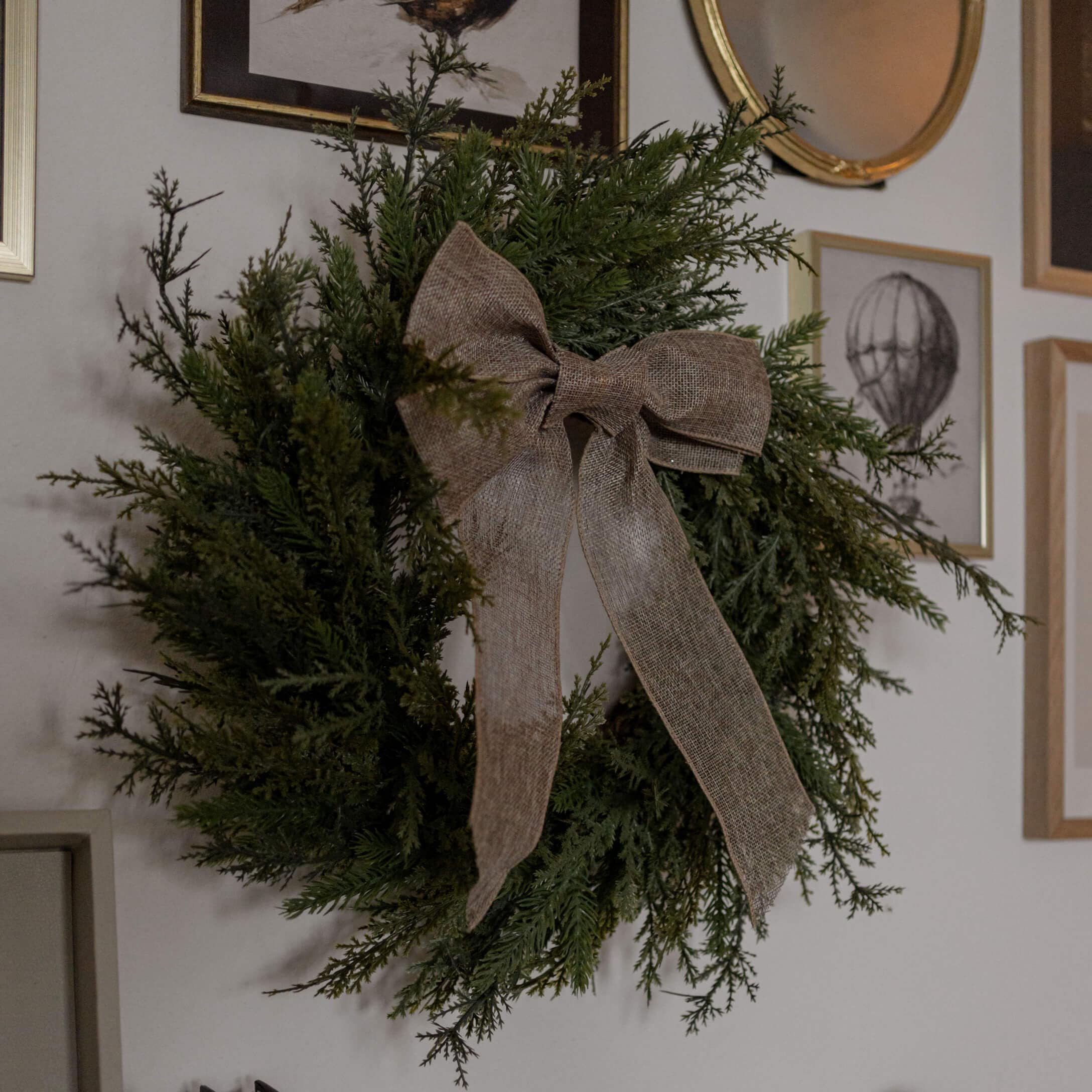 Couronne décorative en branches vertes avec un nœud en toile de jute marron accrochée au mur