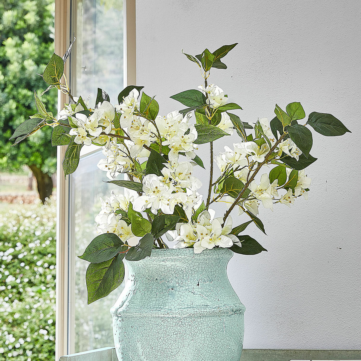 Lot de 6 fleurs décoratives Nireval Fleurs blanches dans un vase en céramique vert clair craquelé devant une fenêtre et un mur blanc