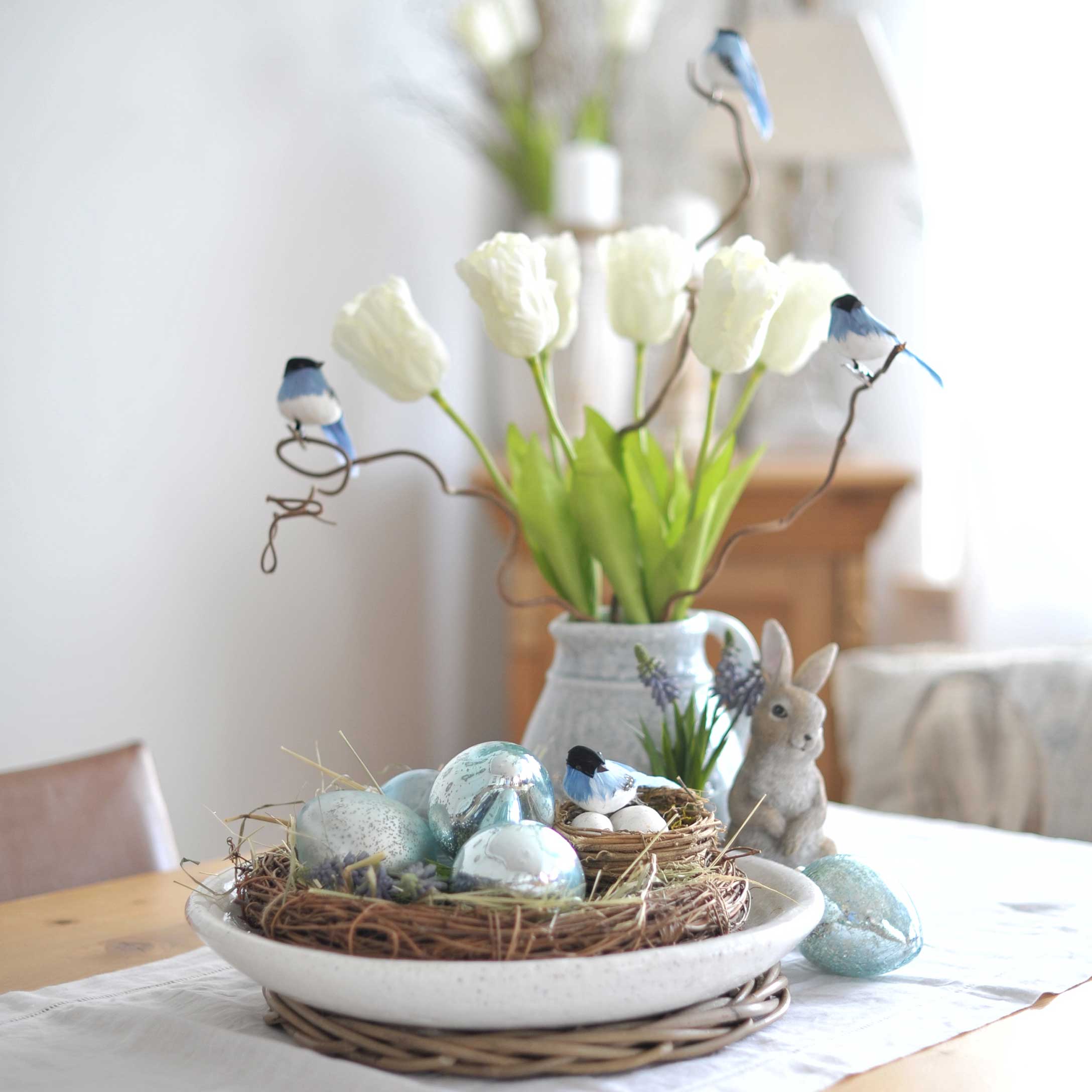 Couronne décorative avec œufs bleus et oiseaux sur table avec tulipes blanches et figurine de lapin