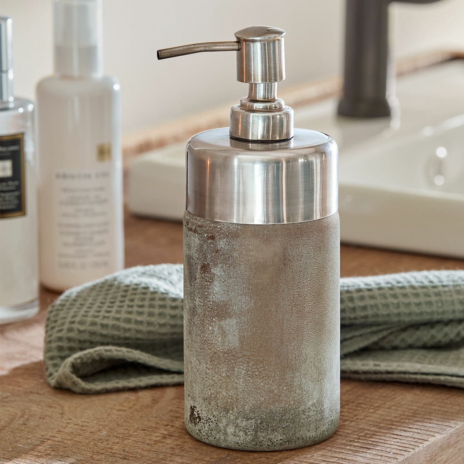 Distributeur de savon avec pompe en métal et base en béton gris sur un comptoir en bois de salle de bain