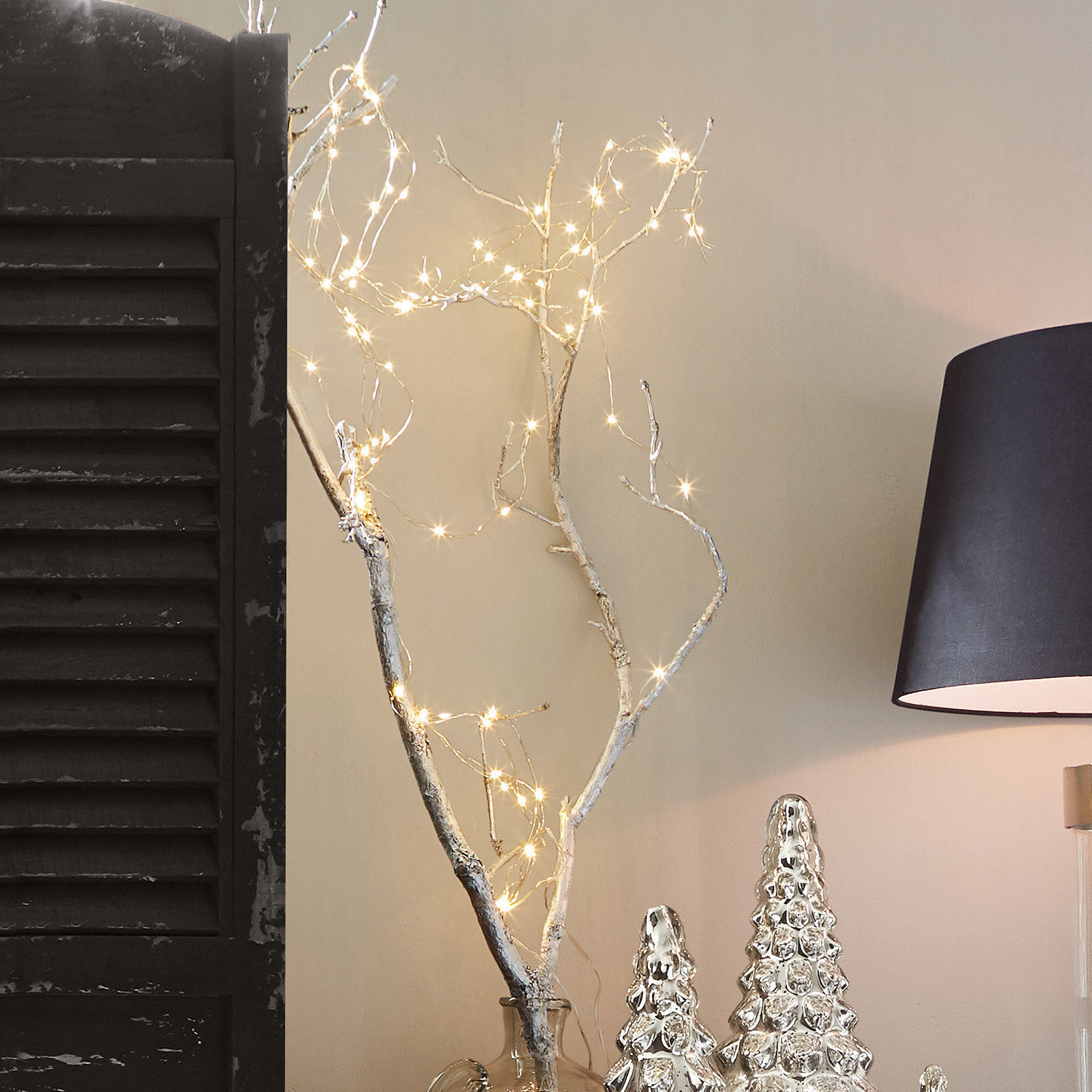 Guirlande lumineuse Loperhet Branche décorative avec guirlande LED dans un vase transparent à côté de décorations argentées et d'une lampe noire