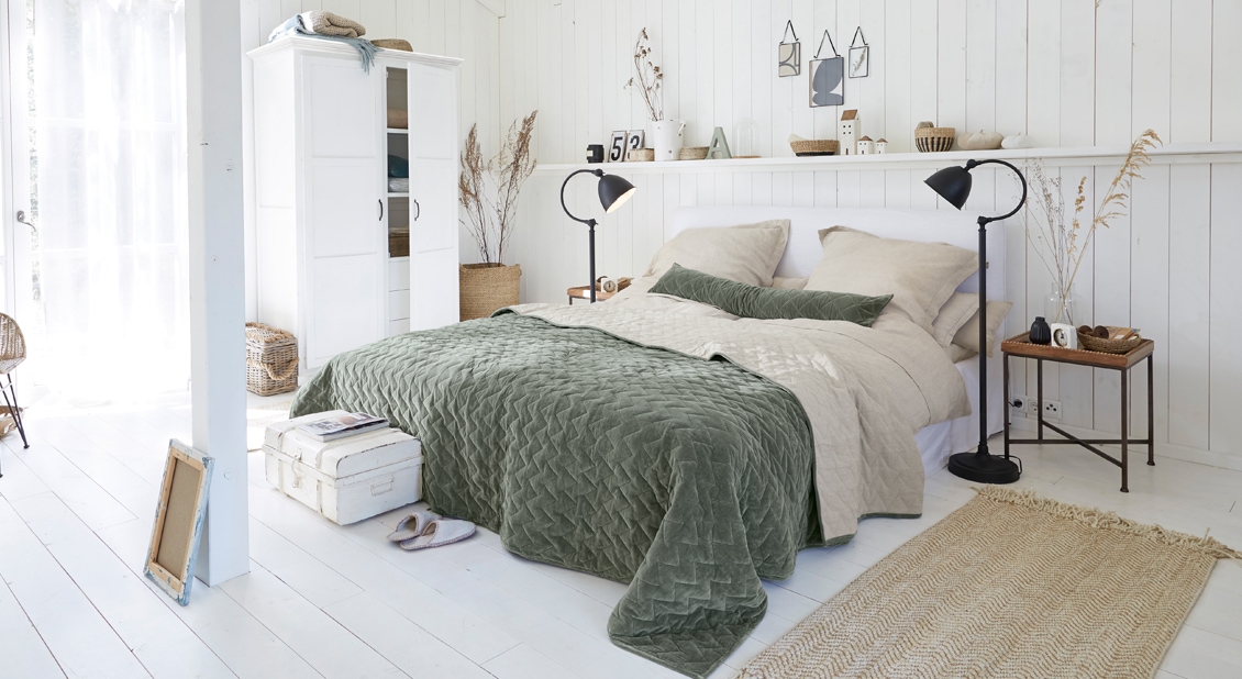 Chambre chaleureuse avec armoire blanche et lit avec couverture matelassée verte et linge de lit beige