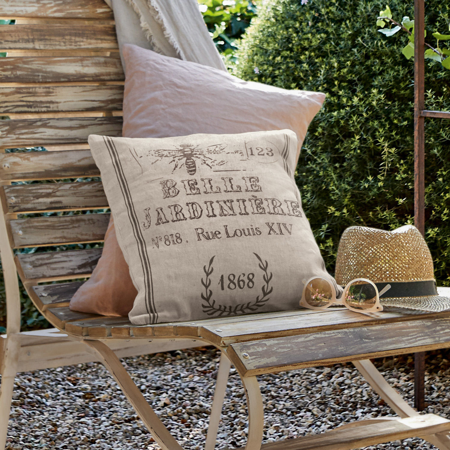 Housse de coussin Abelle Coussin décoratif en lin beige avec impression vintage sur banc en bois dans un jardin extérieur