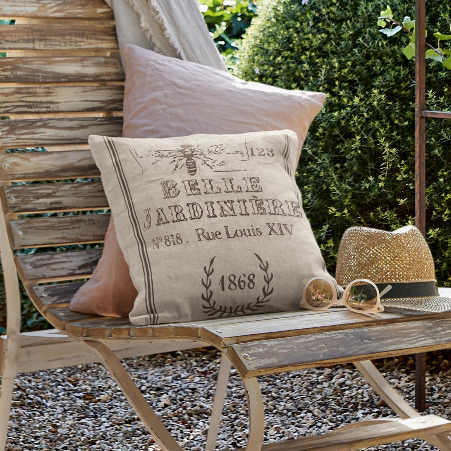 Housse de coussin Abelle Coussin décoratif en lin beige avec impression vintage sur banc en bois dans un jardin extérieur