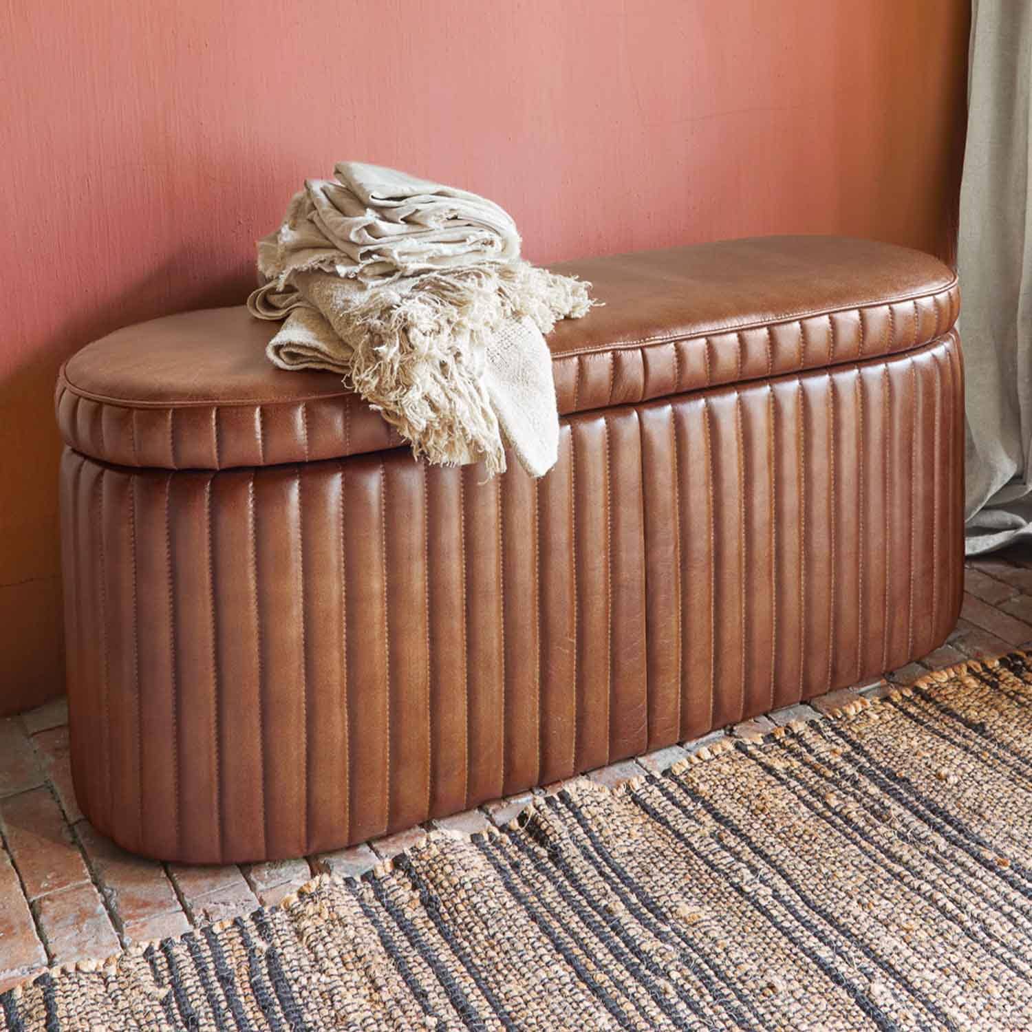 Pouf en cuir marron matelassé avec couvertures crème sur fond de mur rose et tapis
