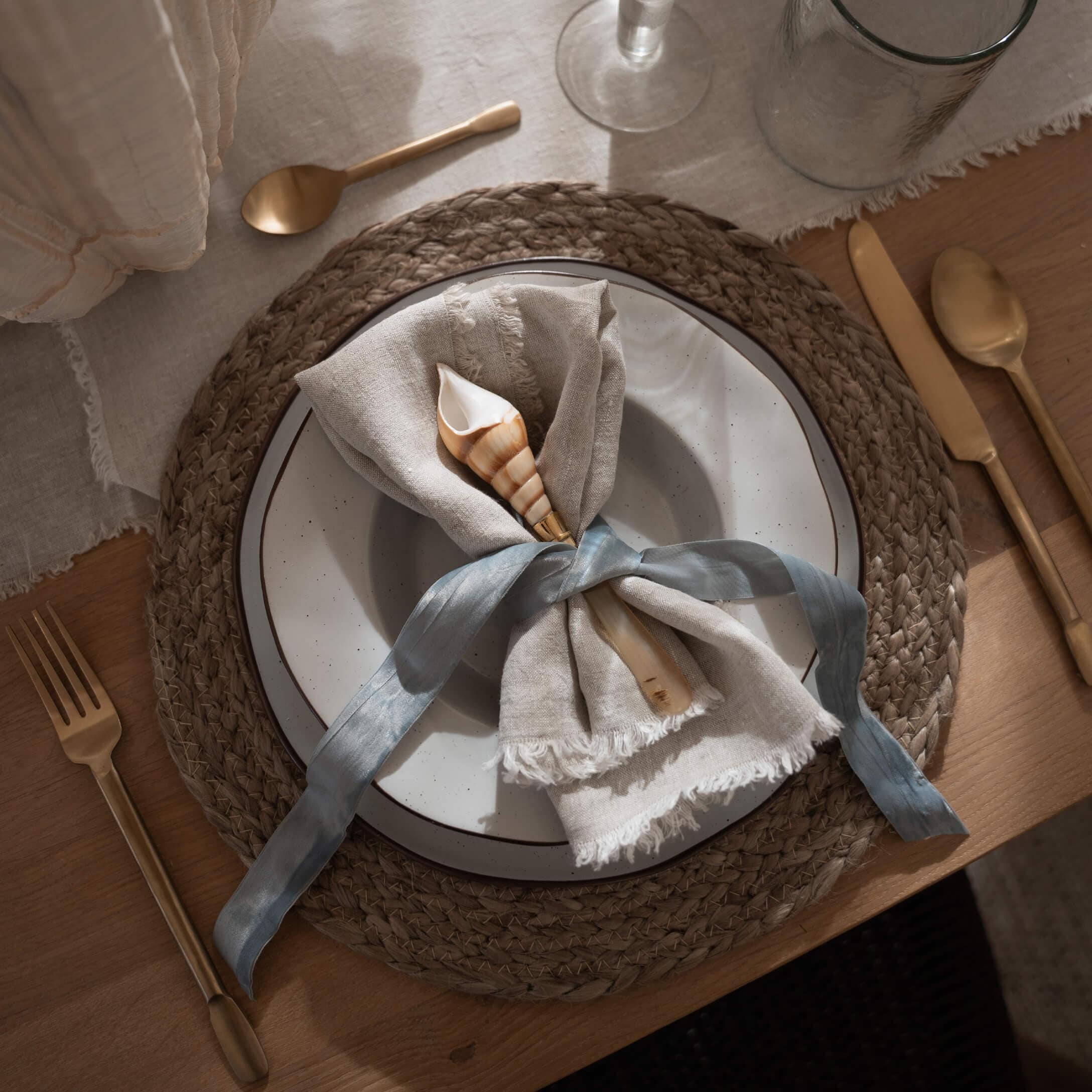 Service de table rustique avec serviette en lin et coquillage sur dessous de plat tressé en matière naturelle