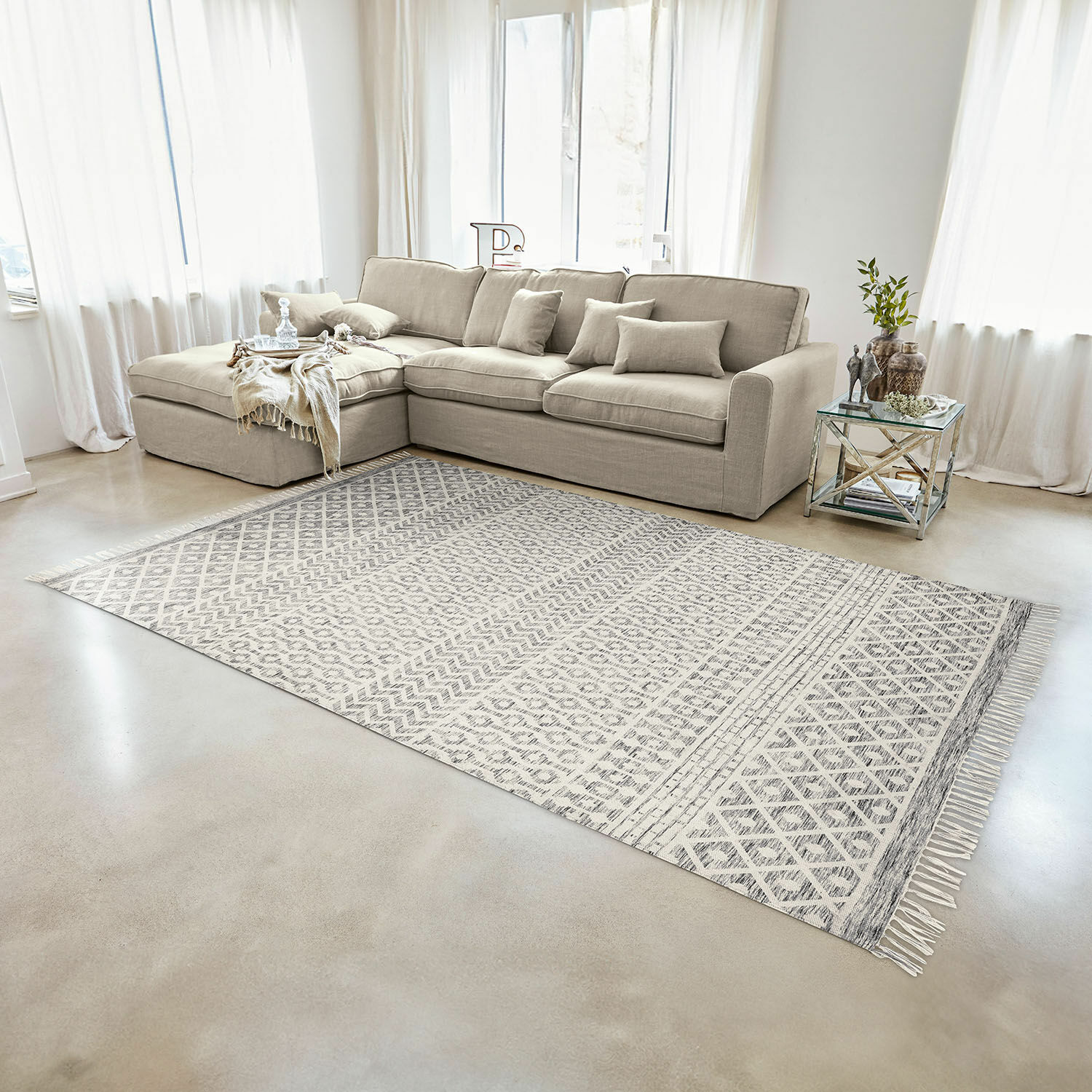 Canapé d'angle beige en tissu dans un salon lumineux avec tapis à motifs géométriques et table en verre