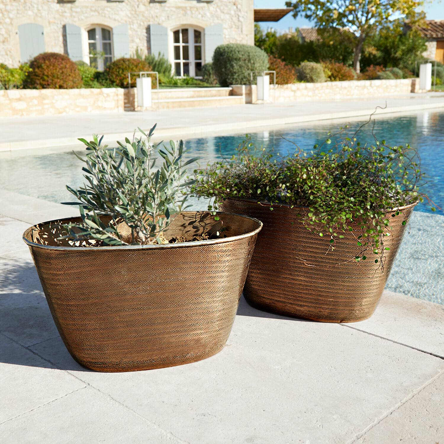 Lot de 2 cache-pots Rinalo Deux jardinières en cuivre avec plantes près d'une piscine sur une terrasse en pierre, décoration extérieure