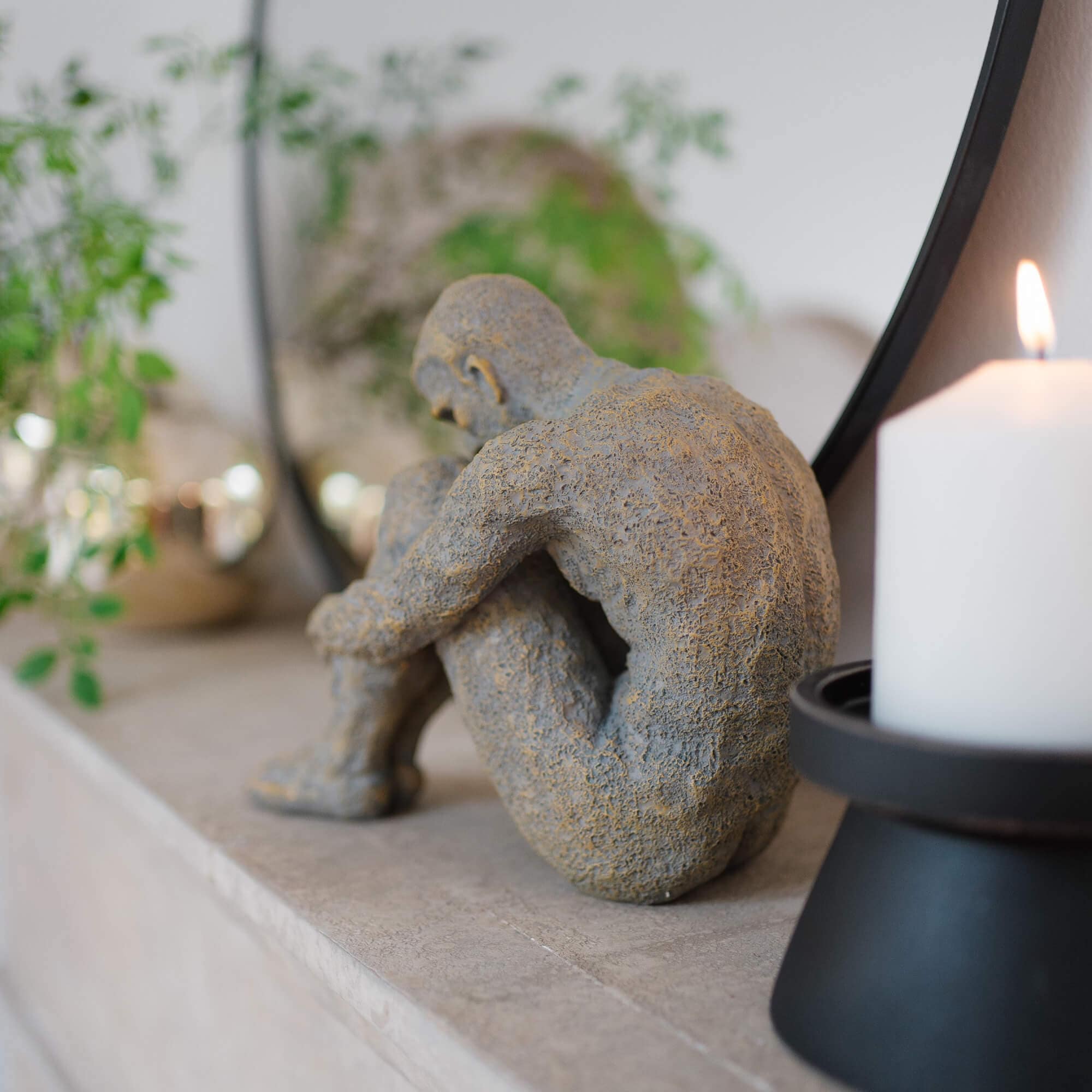 Sculpture en pierre grise d'une figure assise sur une étagère en marbre avec une bougie blanche