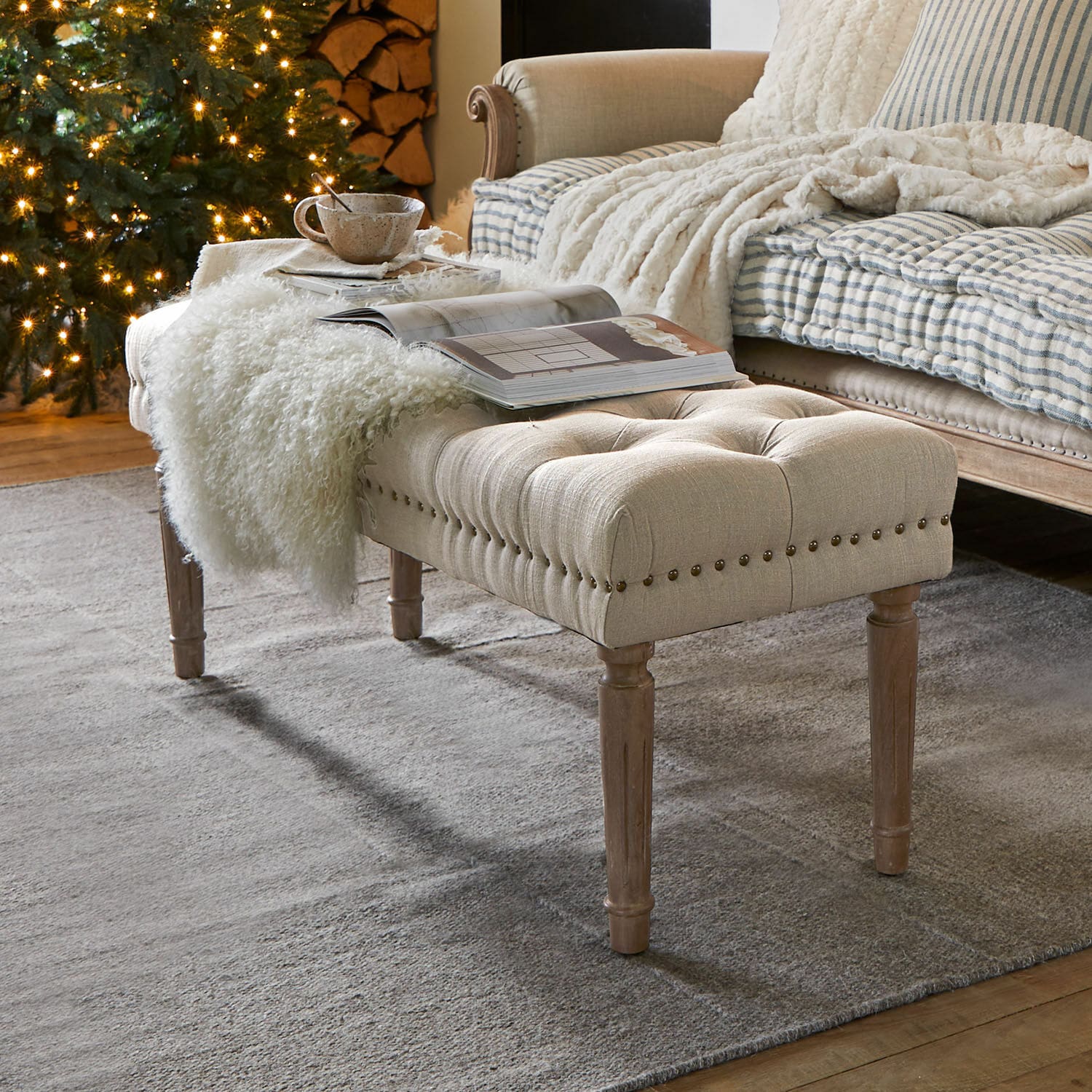Banquette Brookfield Banc capitonné beige avec pieds en bois sur tapis gris dans un salon chaleureux avec sapin décoré