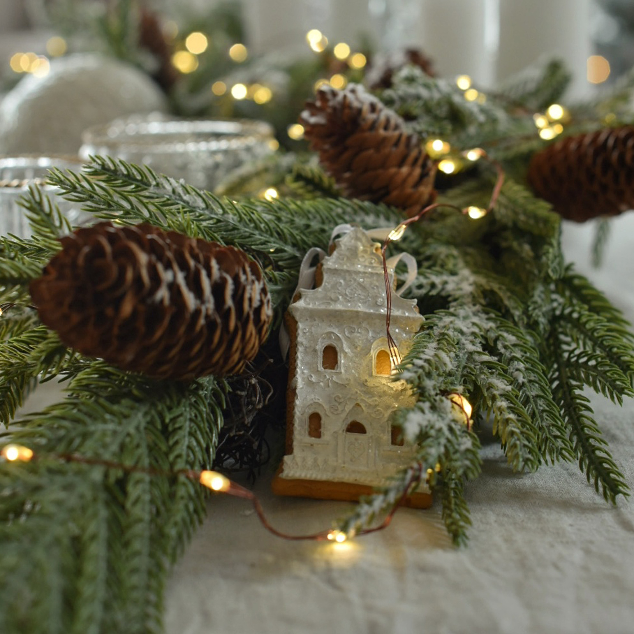 Décoration de Noël avec branches vertes, pommes de pin et maison en pain d'épice illuminée sur table