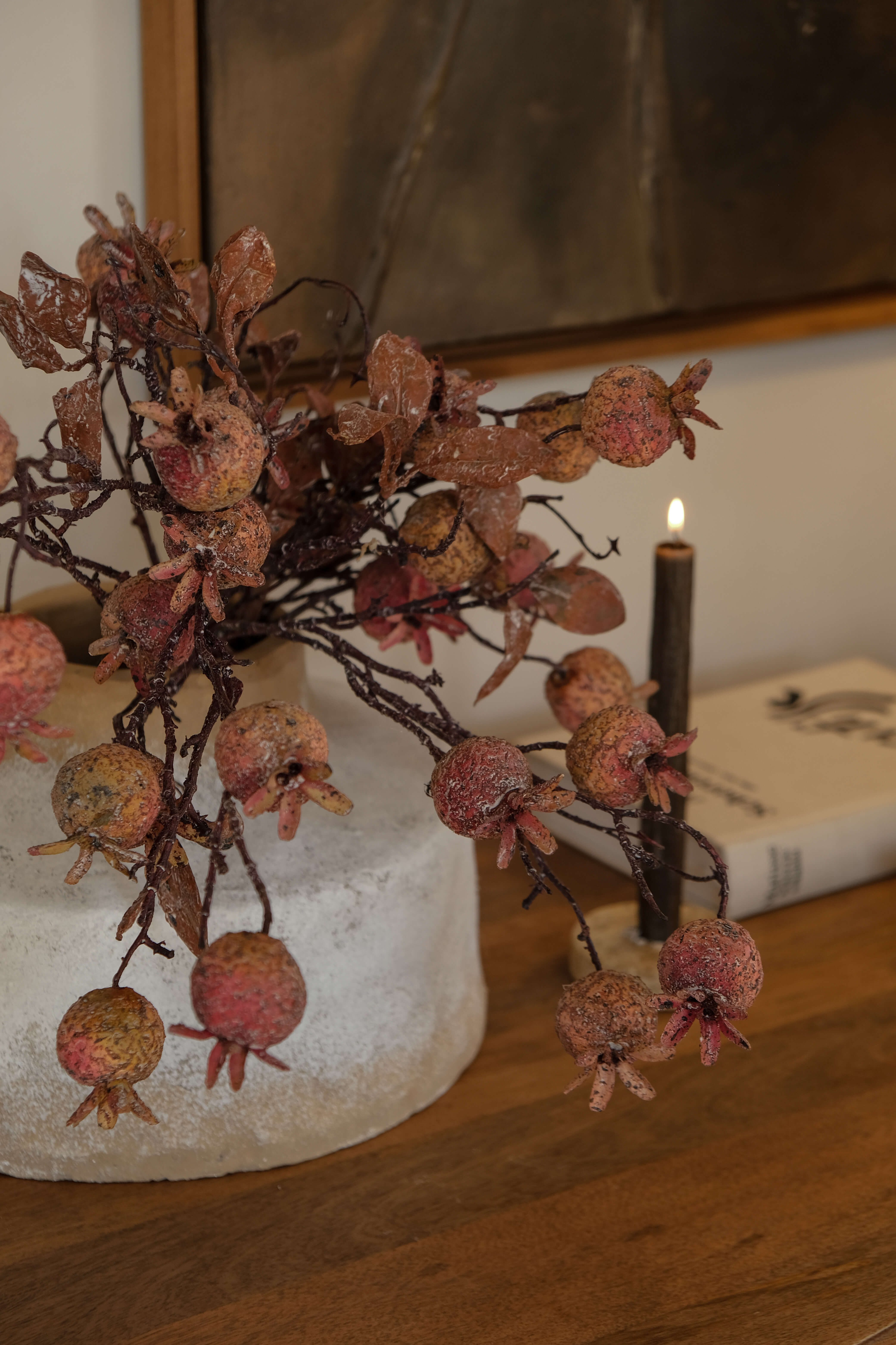 Branche décorative avec fruits de grenade en tons naturels sur socle clair posée sur une table en bois