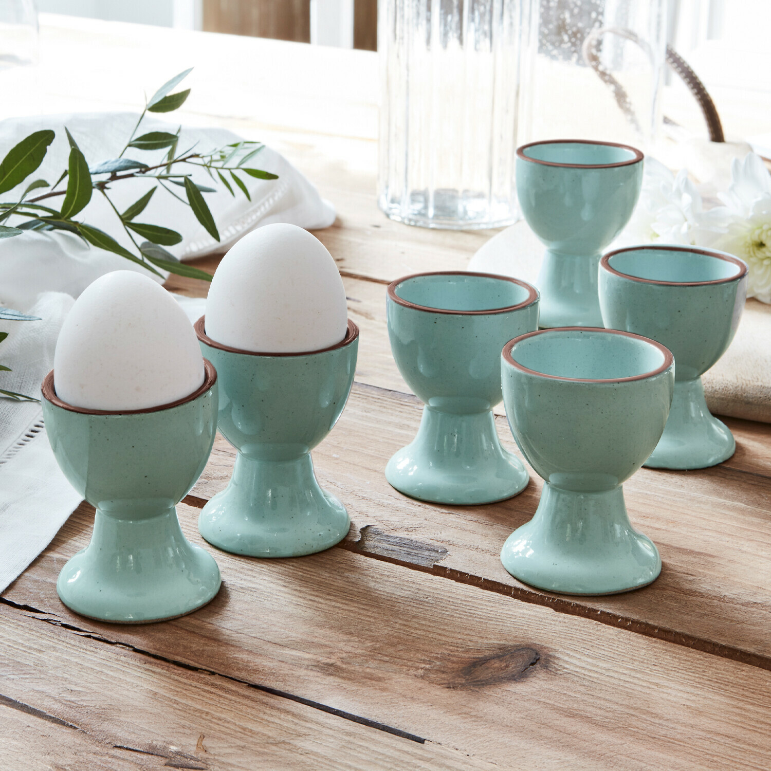 Lot de 6 coquetiers Biarré Ensemble de six coquetiers en céramique bleu clair avec bord brun sur table en bois rustique