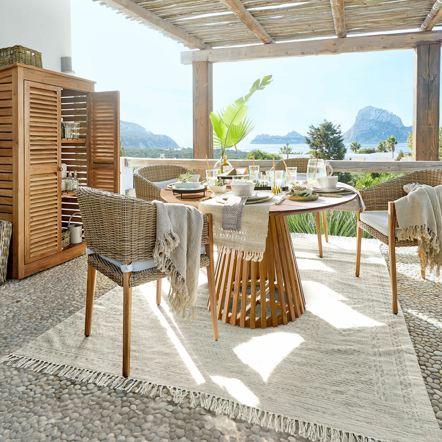 Tapis d'extérieur Savagnac Salle à manger extérieure avec table en bois et chaises en osier beige, vue sur la mer et montagne