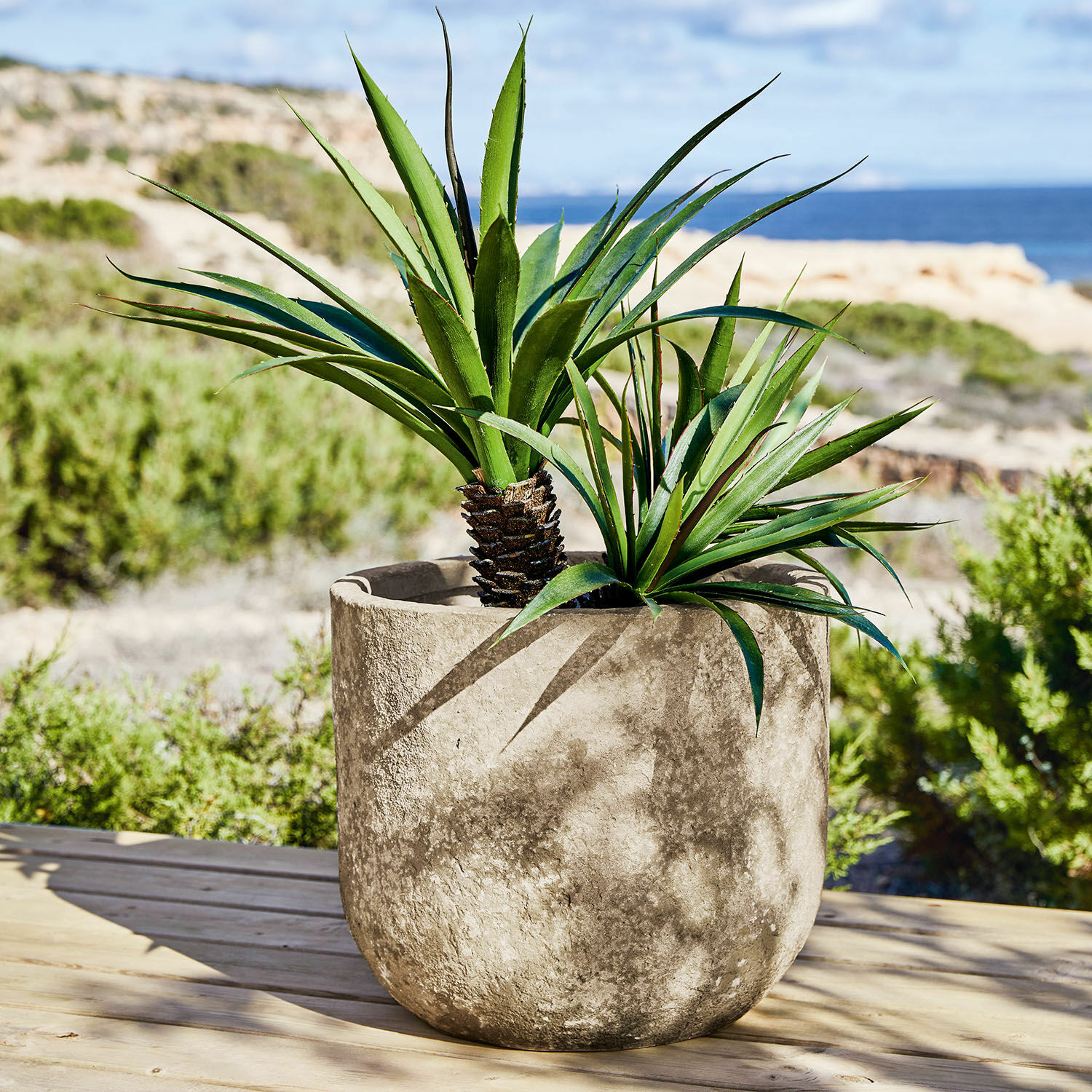 Cache-pot Ela Grand pot en béton gris avec plantes vertes sur terrasse avec vue sur la mer