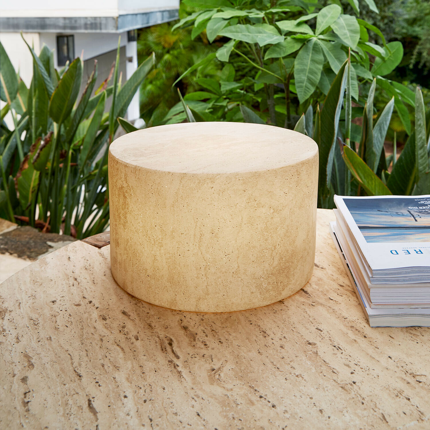 Lampe LED rechargeable Marévos Table ronde en travertin beige sur terrasse avec plantes vertes, mobilier en pierre naturelle