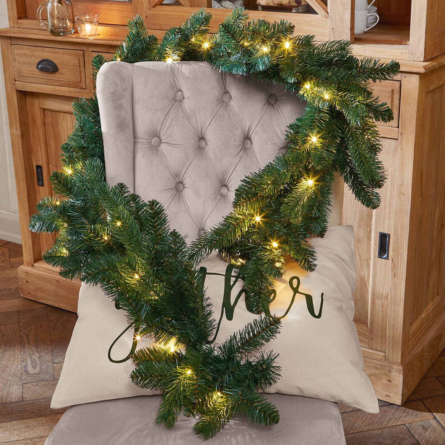 Guirlande LED Monetry Couronne de Noël verte avec lumières LED chaudes posée sur un fauteuil beige capitonné