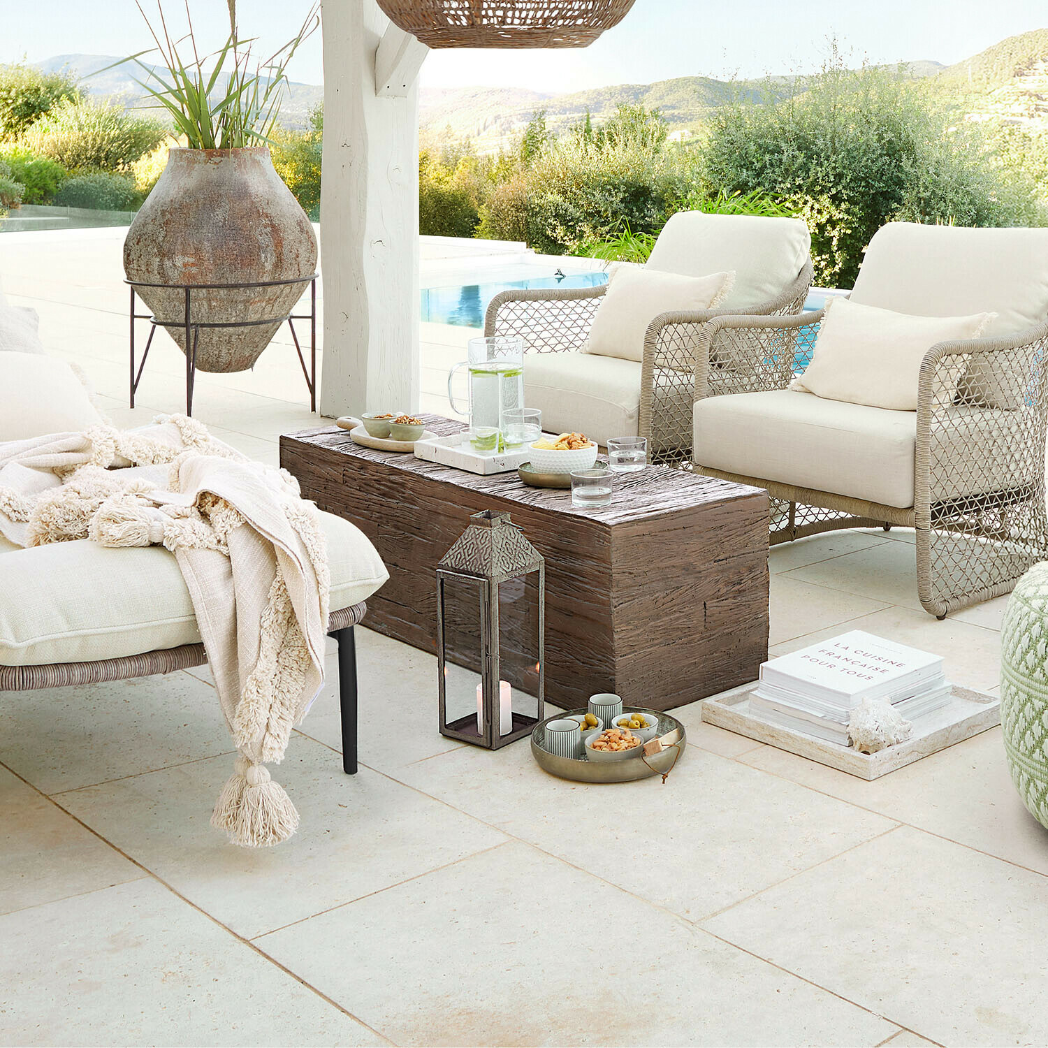 Ensemble de mobilier d'extérieur beige avec coussins et table en bois sur terrasse avec vue piscine et nature