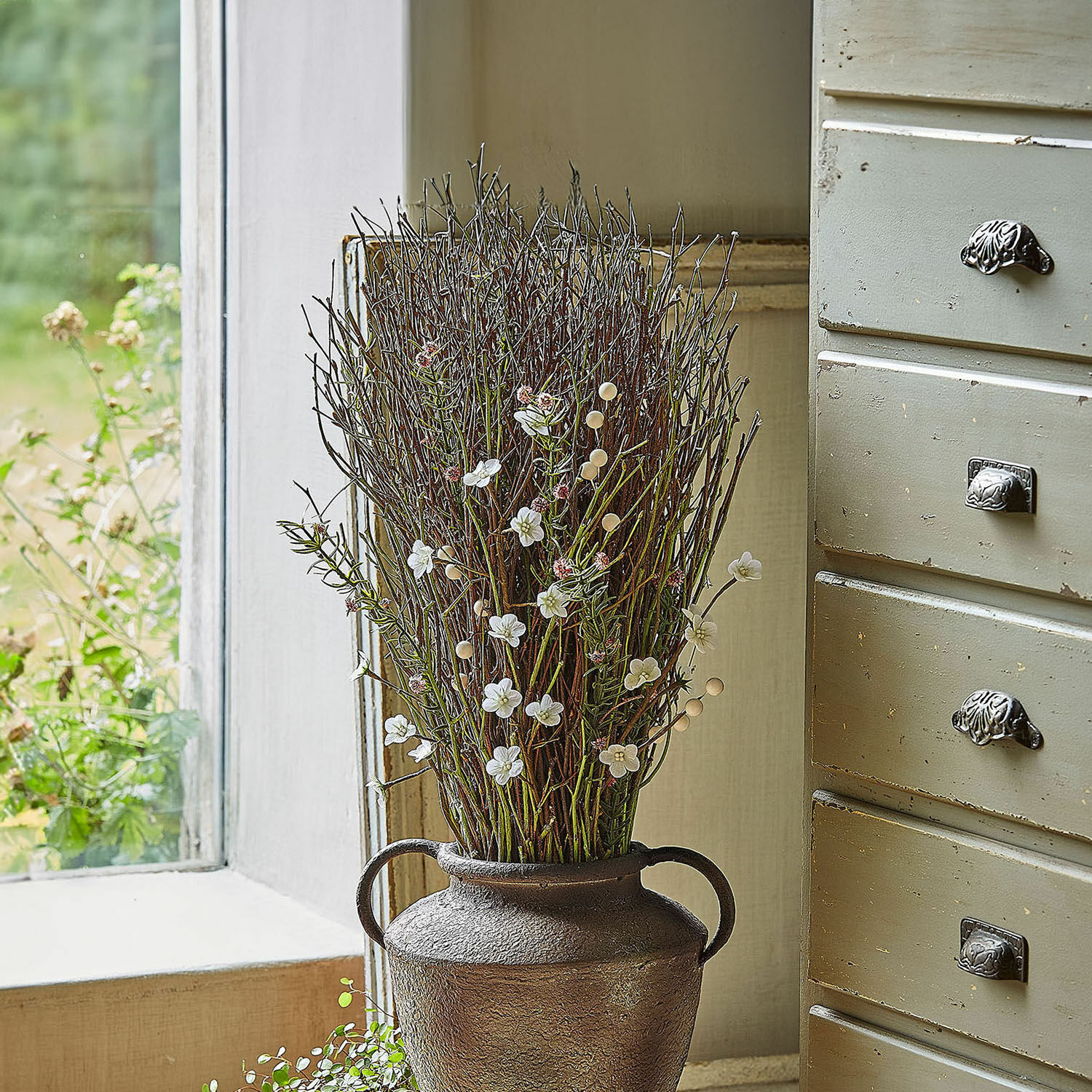 Bouquet décoratif Verilo Vase décoratif en métal brun avec branches et fleurs blanches posé sur un rebord de fenêtre
