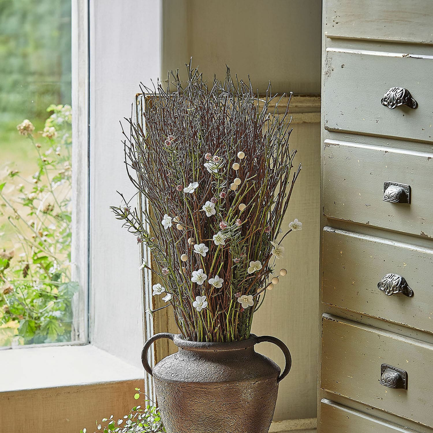 Bouquet décoratif Verilo Vase décoratif en métal brun avec branches et fleurs blanches posé sur un rebord de fenêtre