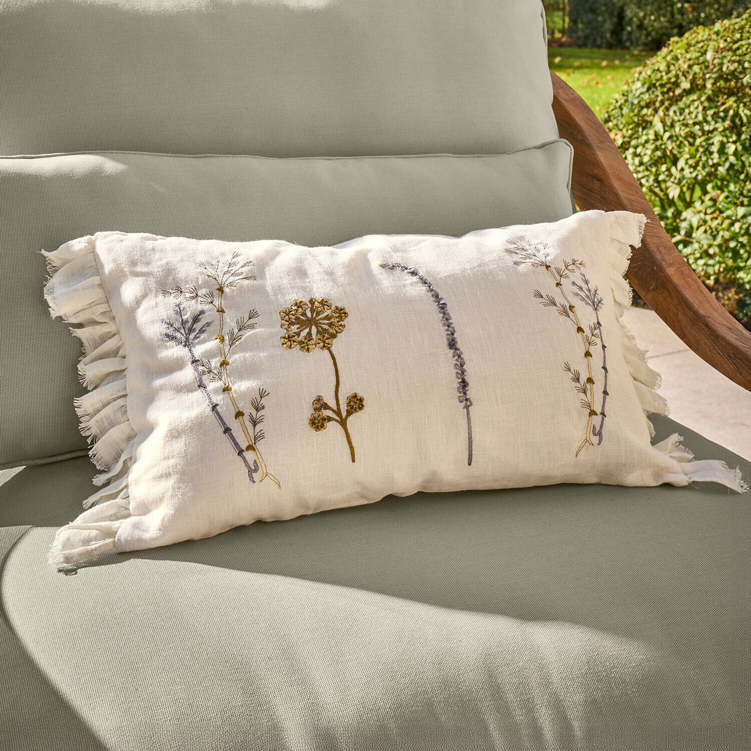 Coussin beige en lin avec broderies florales et franges sur fauteuil de jardin vert