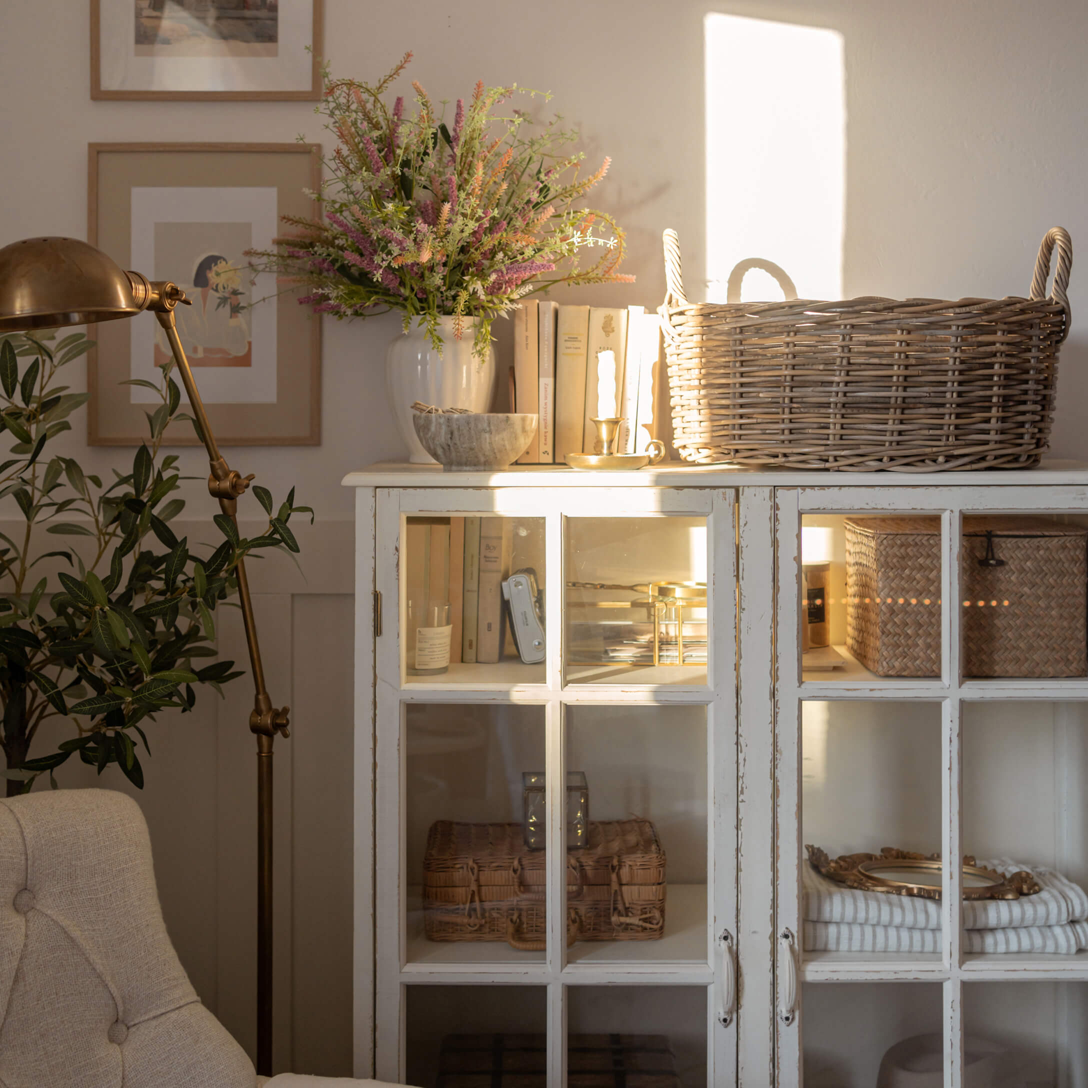 Buffet en bois blanc avec portes vitrées, panier en osier et décorations dans un salon lumineux