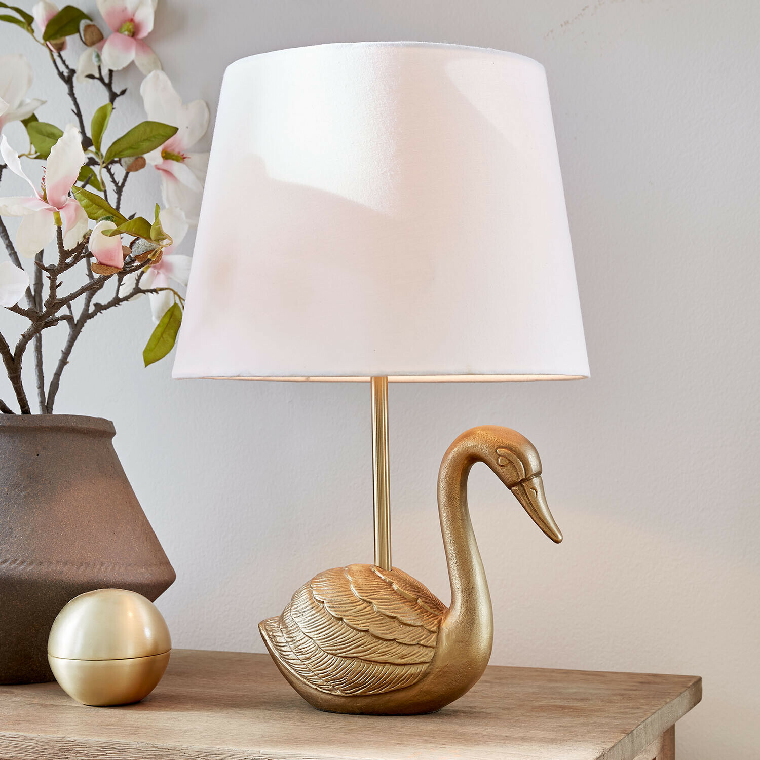 Lampe à poser Élégance Dorée Lampe de table dorée en forme de cygne avec abat-jour blanc sur une table en bois décorée de fleurs