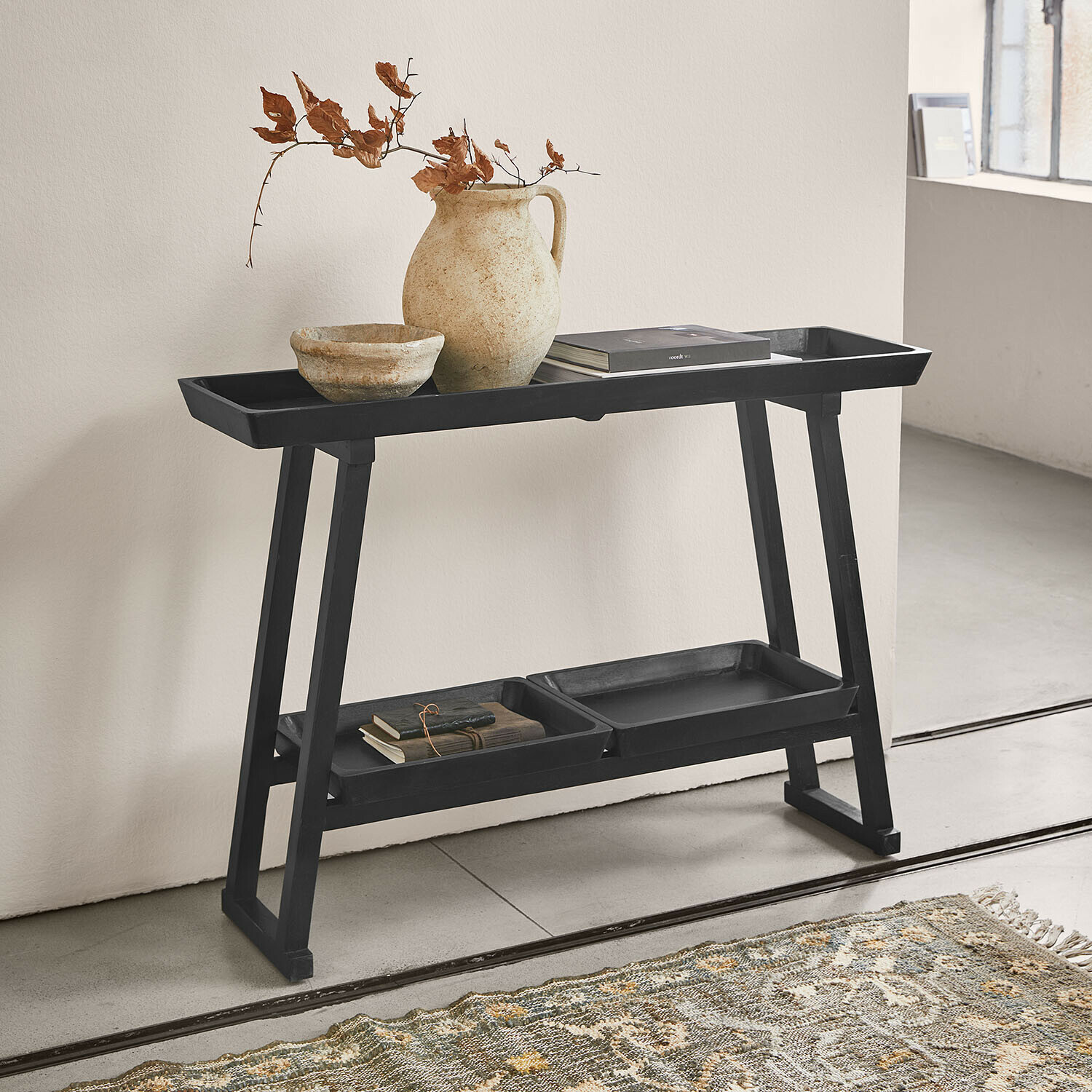 Console Ivywood Table noire en bois avec étagères, vase en céramique et livres dans un intérieur minimaliste