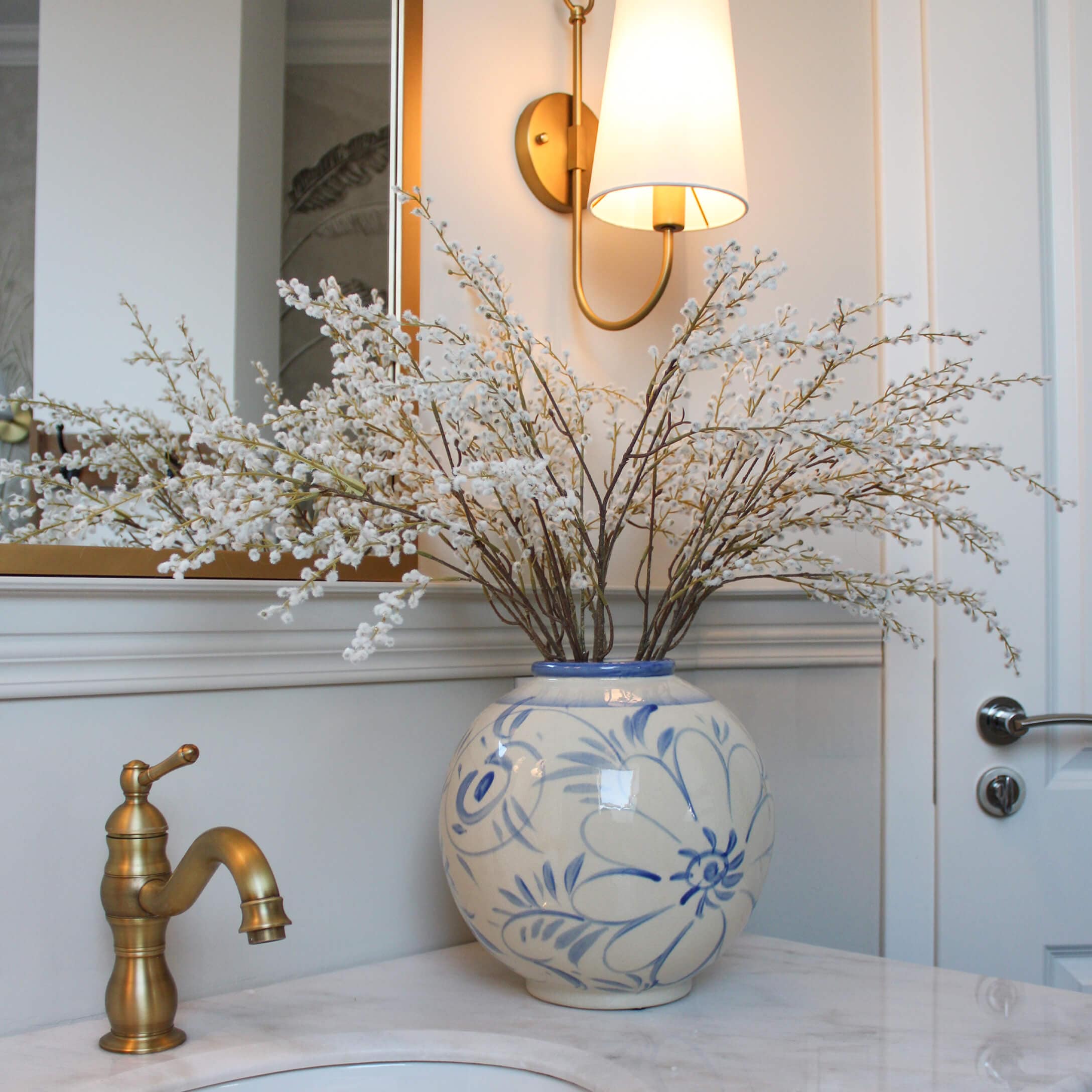 Vase en céramique avec motif floral bleu et branches de fleurs blanches sur un comptoir en marbre de salle de bain