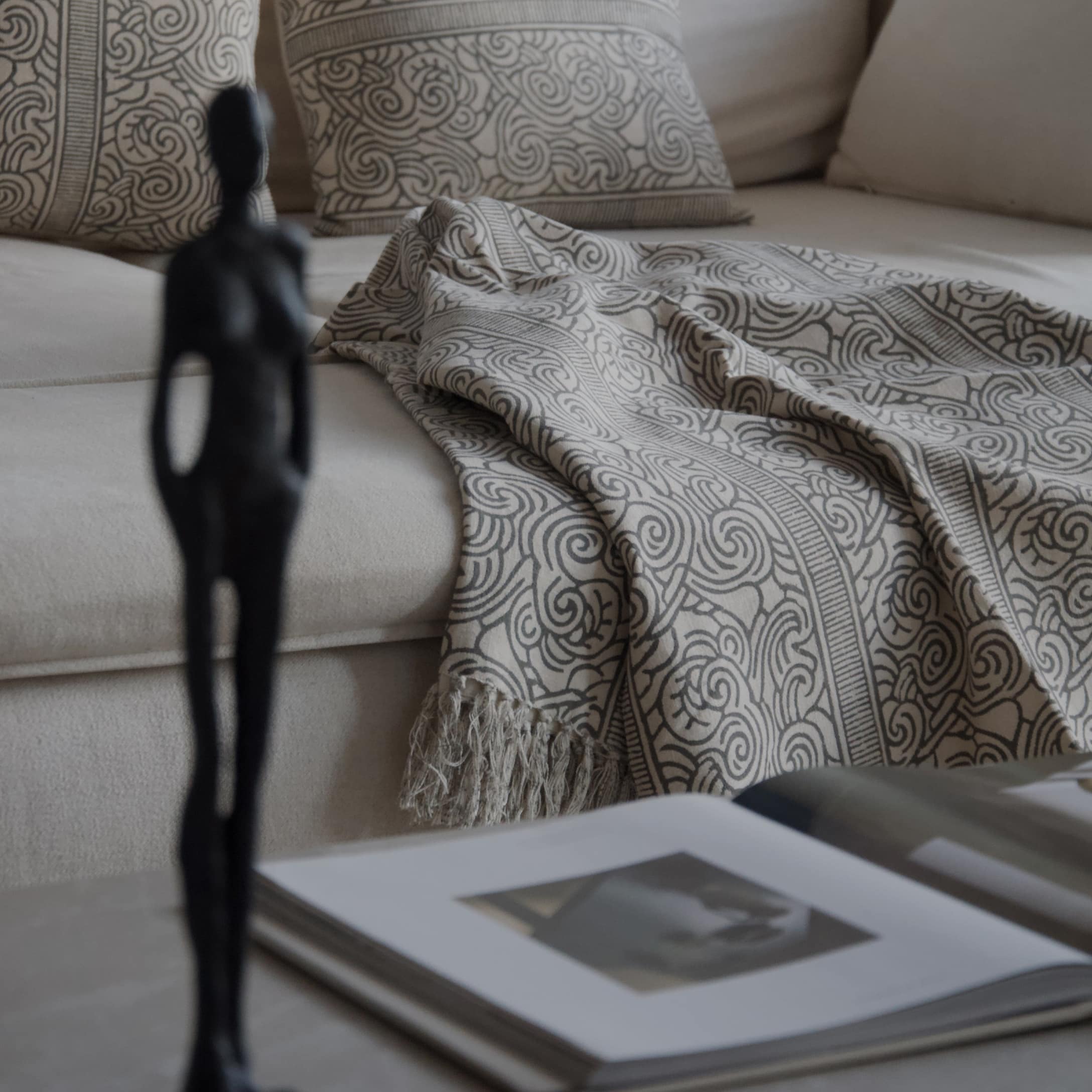 Plaid décoratif beige avec motif gris sur canapé clair, coussins assortis et livre ouvert