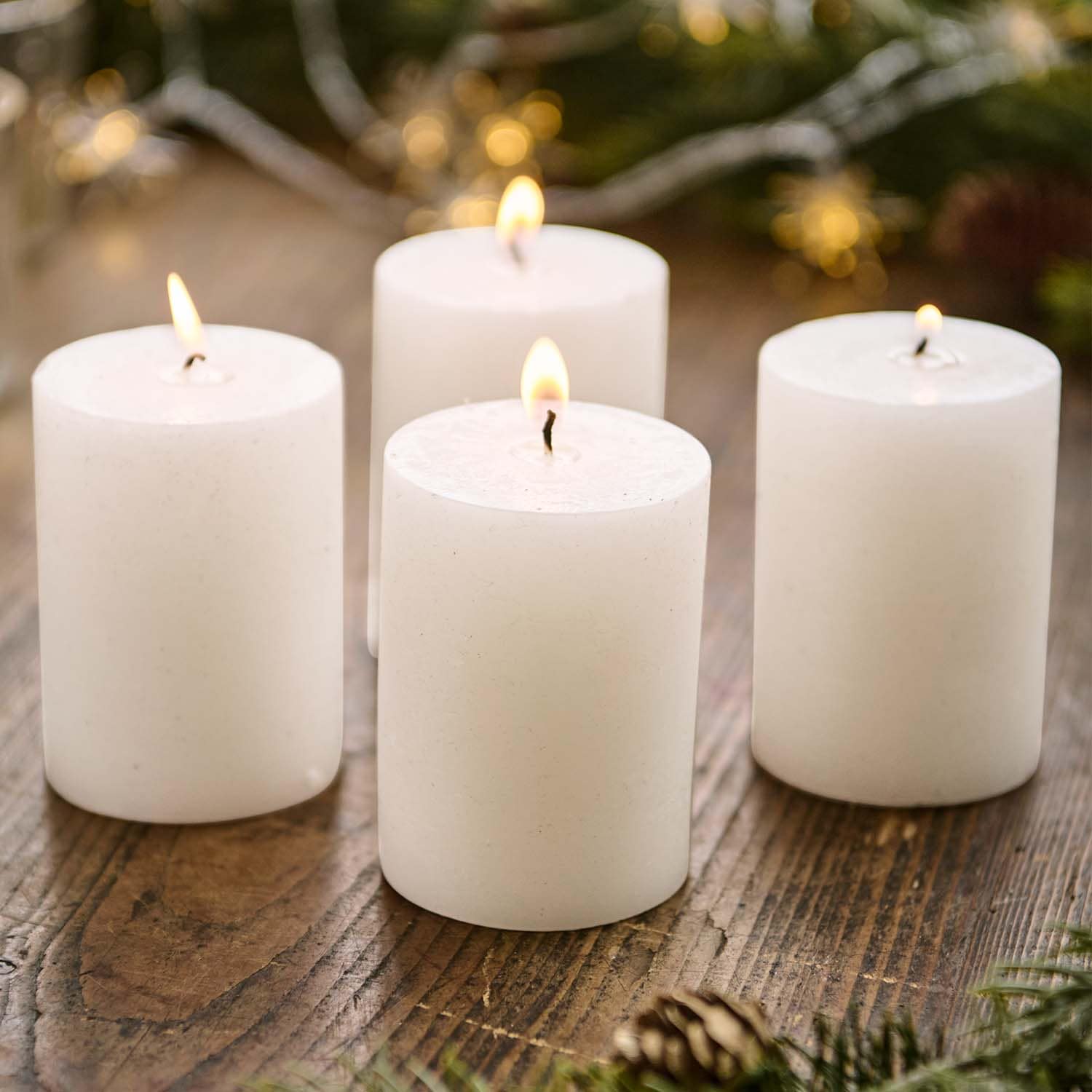 Ensemble de quatre bougies blanches cylindriques allumées sur une table en bois avec décorations festives