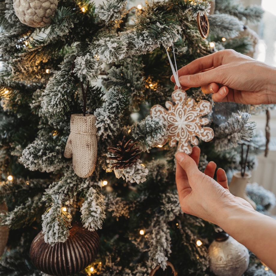 Mains accrochant un flocon de neige sur un sapin enneigé décoré de lumières et ornements de Noël