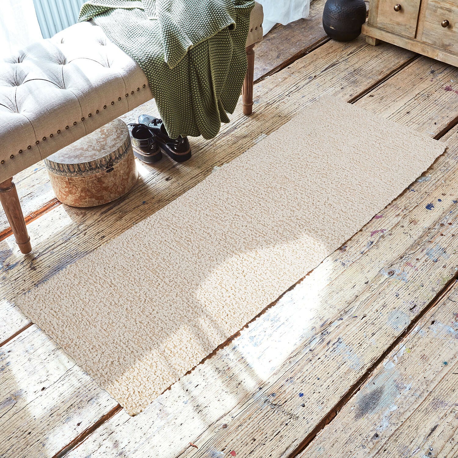 Tapis Kaleema Tapis beige en tissu doux sur un sol en bois dans un intérieur chaleureux avec un banc et une couverture verte