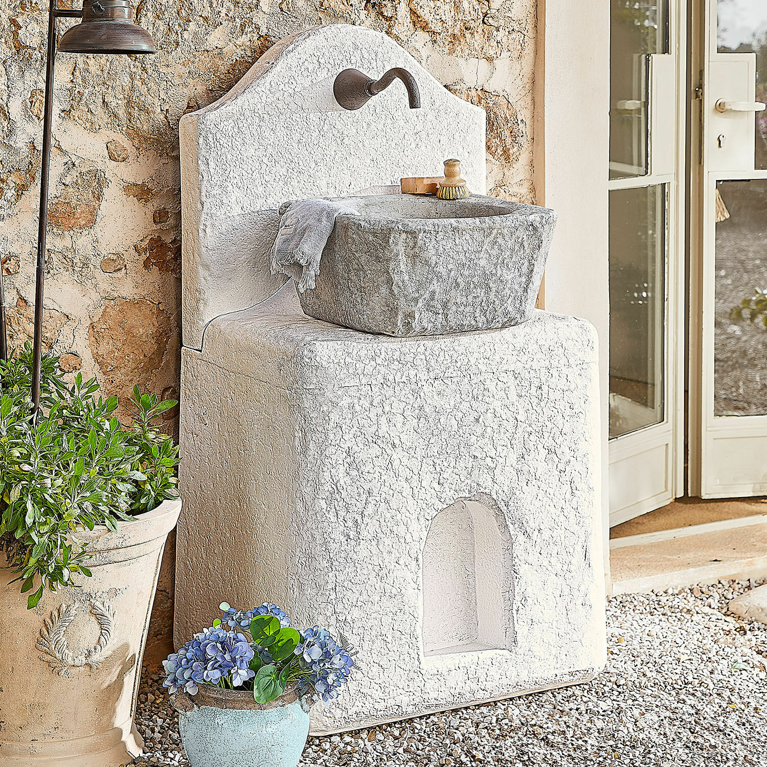 Fontaine Pisticci Évier de jardin en pierre blanche avec bassin gris et robinet en métal, décor extérieur avec plantes