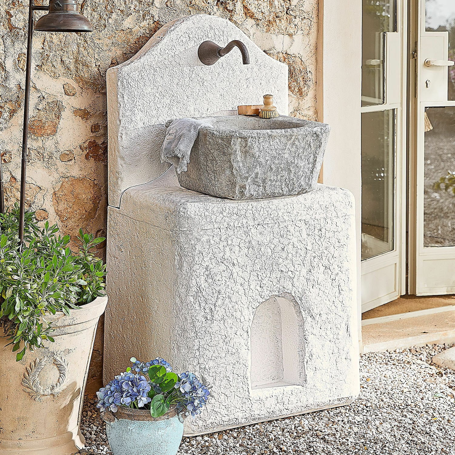 Fontaine Pisticci Évier de jardin en pierre blanche avec bassin gris et robinet en métal, décor extérieur avec plantes
