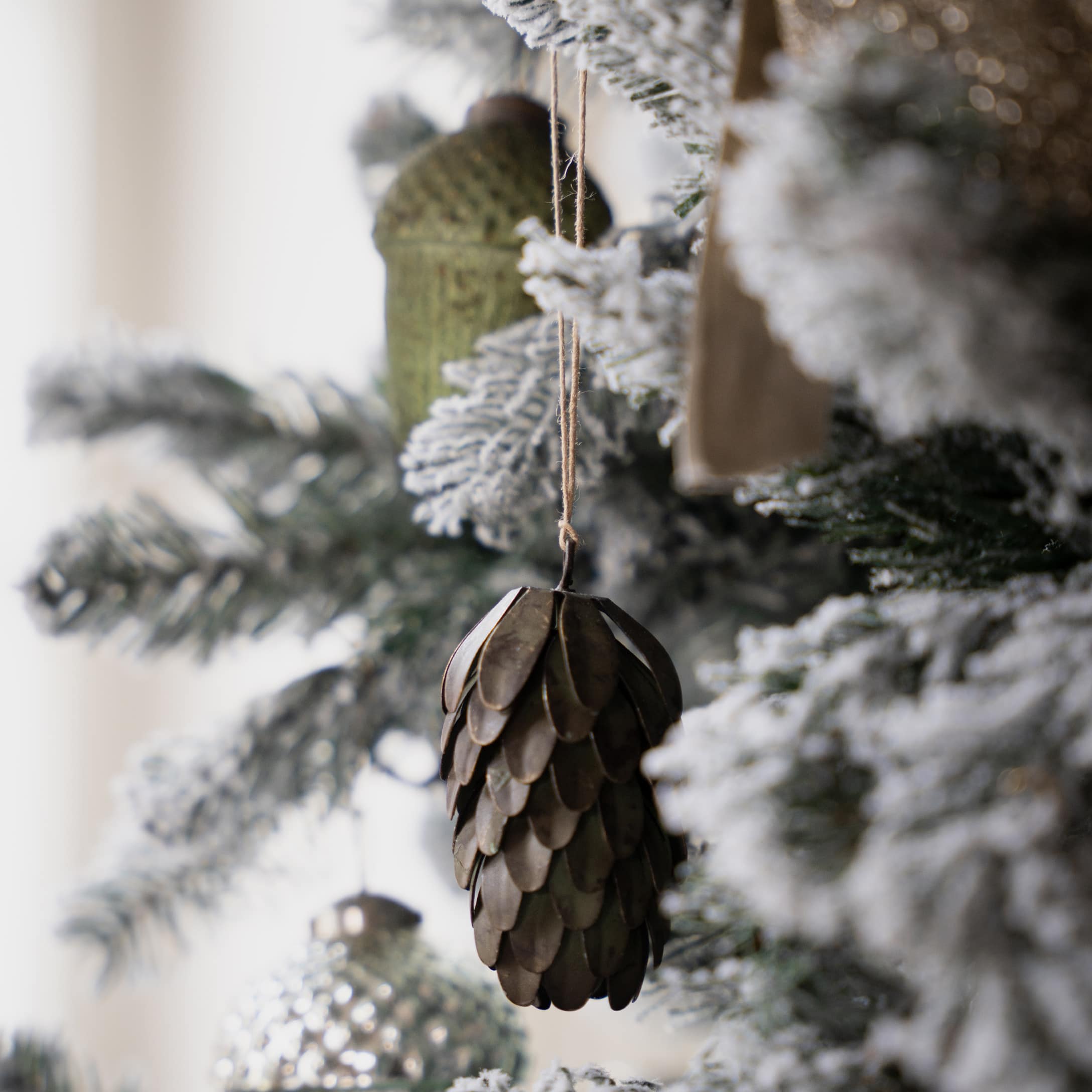 Décoration de sapin en forme de pomme de pin en métal brun sur branches enneigées