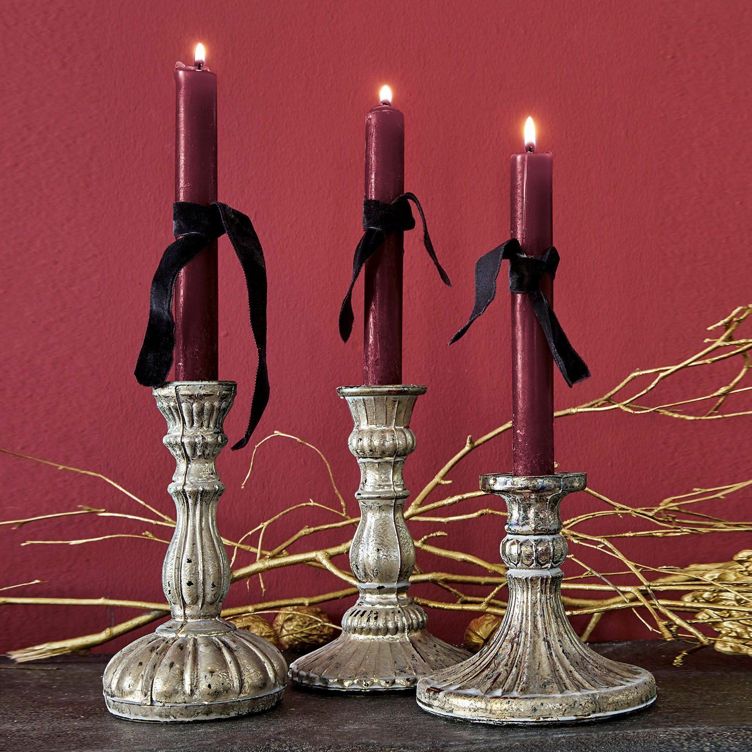 Trois bougeoirs en métal décoratif avec bougies bordeaux et rubans noirs sur fond sombre